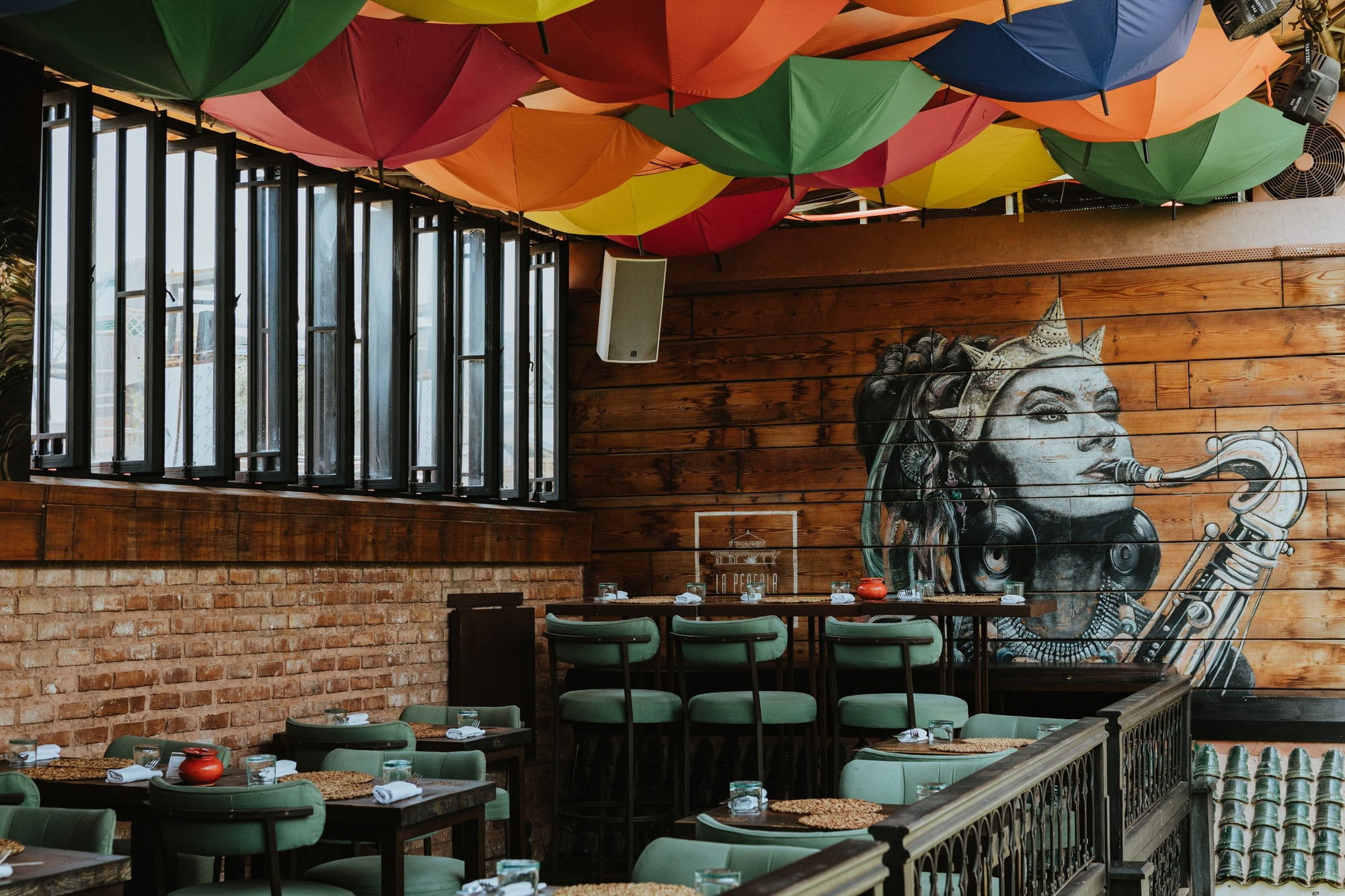 Dining terrace at La Pergola with a ceiling of colourful umbrellas and a mural of a saxophone player