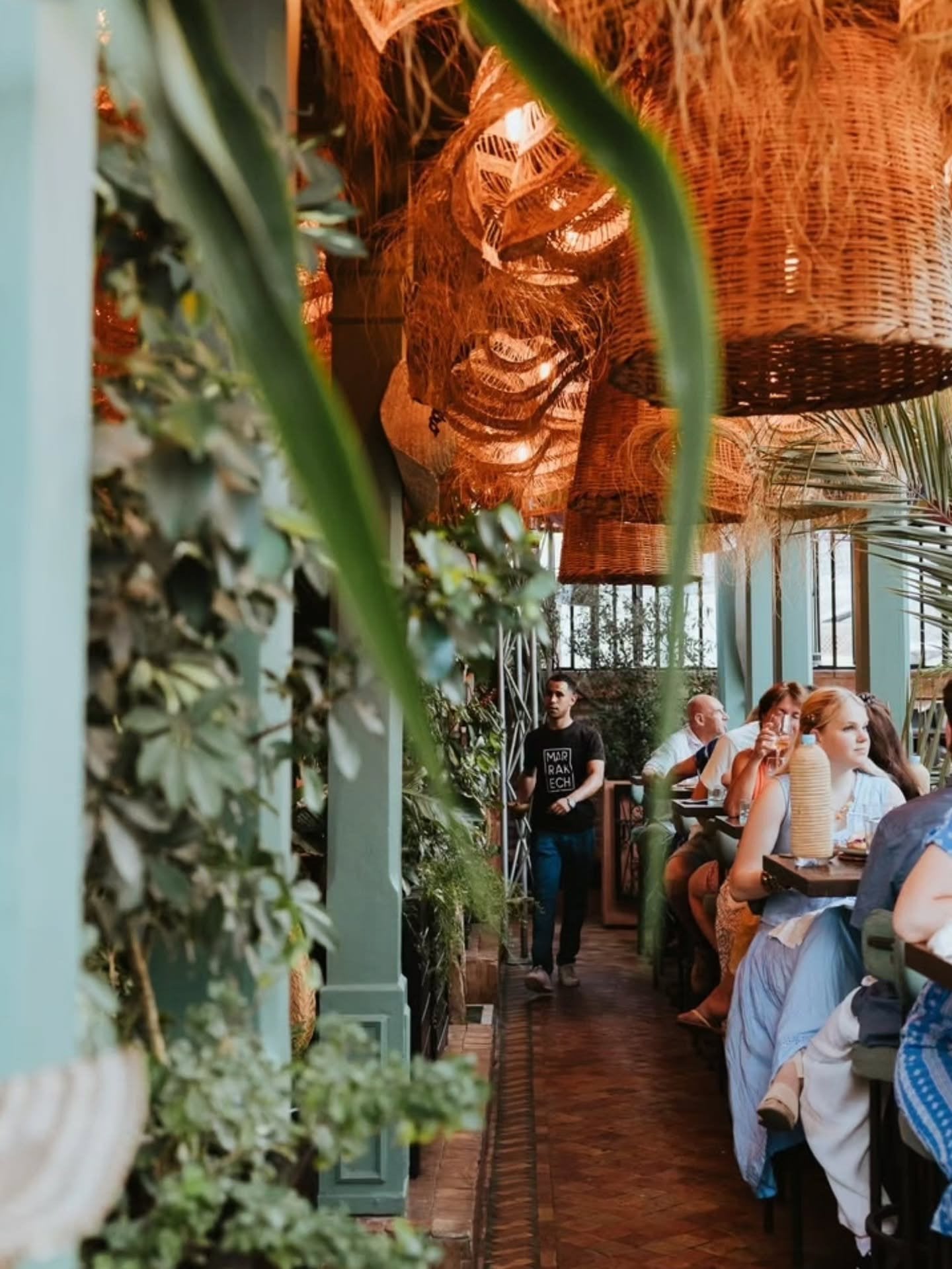 Covered walkway at La Pergola lined with plants and wicker lamps, guests seated at tables