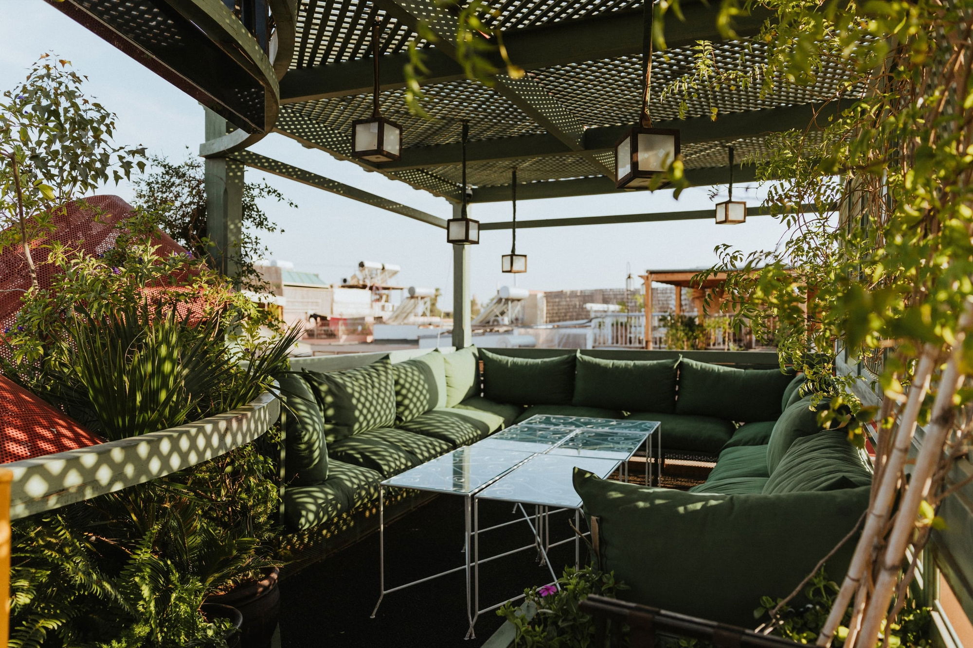 Green lounge sofas under a lattice pergola on the La Pergola rooftop, medina roofs behind