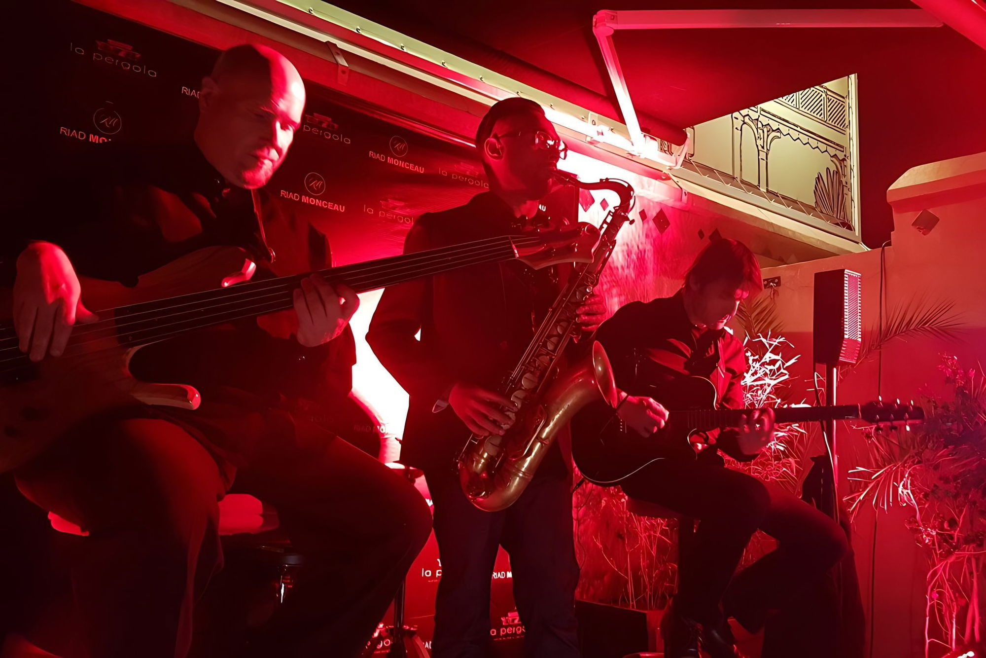A jazz trio with bass, saxophone and guitar playing under red lights at La Pergola