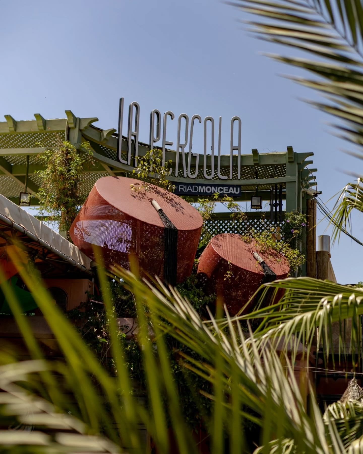 The La Pergola sign above the rooftop garden of Riad Monceau, with palm fronds in front