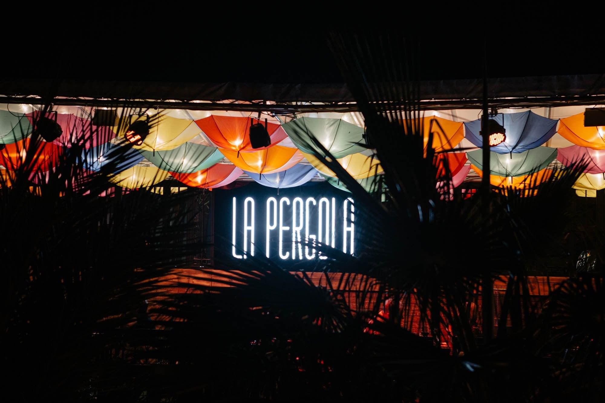 Neon La Pergola sign under a ceiling of colourful umbrellas at night
