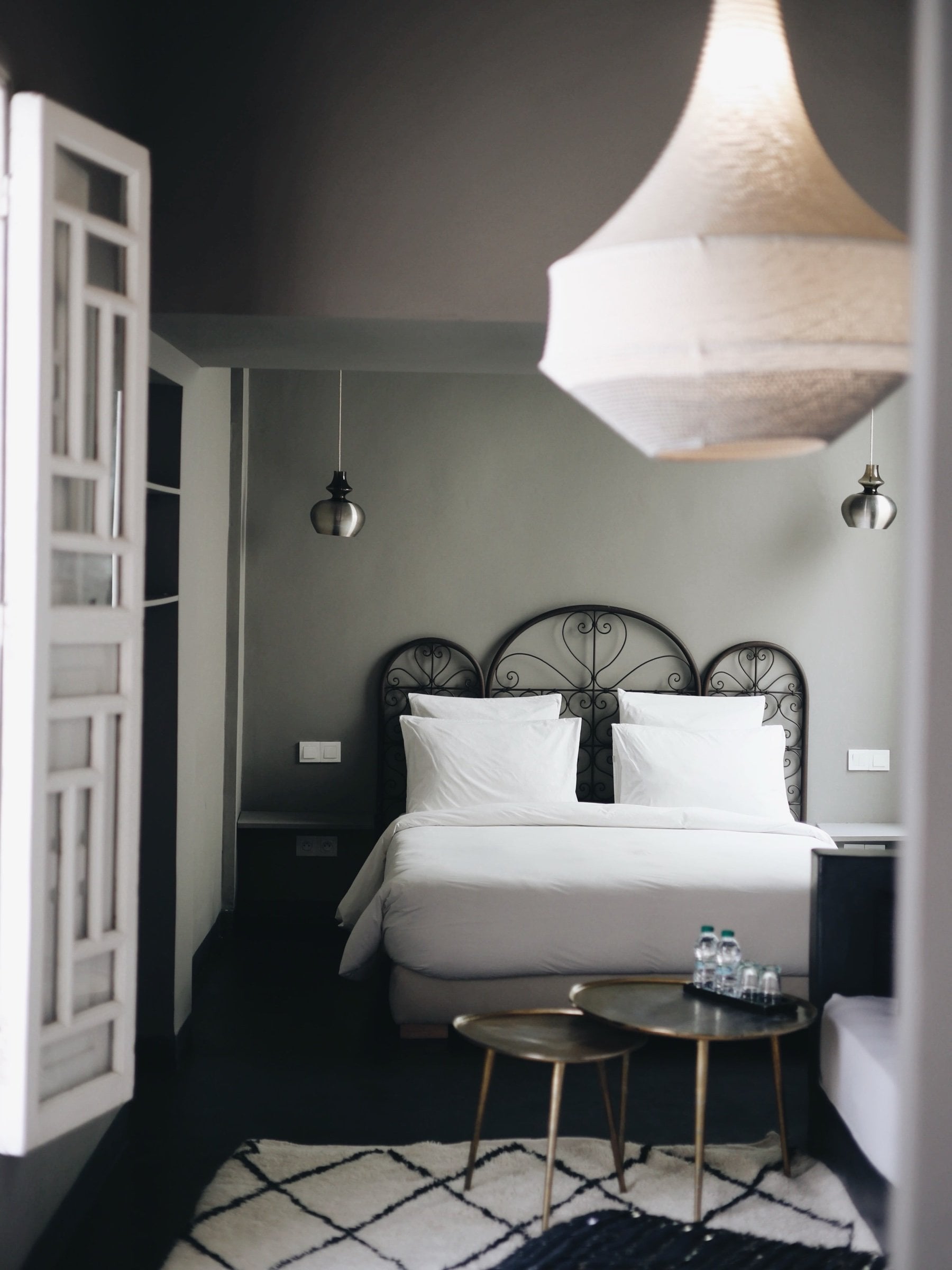 Suite at Numa Marrakech with an iron headboard, a white pendant lamp, a Berber rug and carved shutters