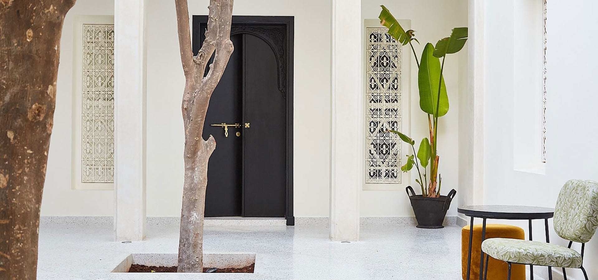 Courtyard of Numa Marrakech with an orange tree trunk, a black arched door and carved white screens