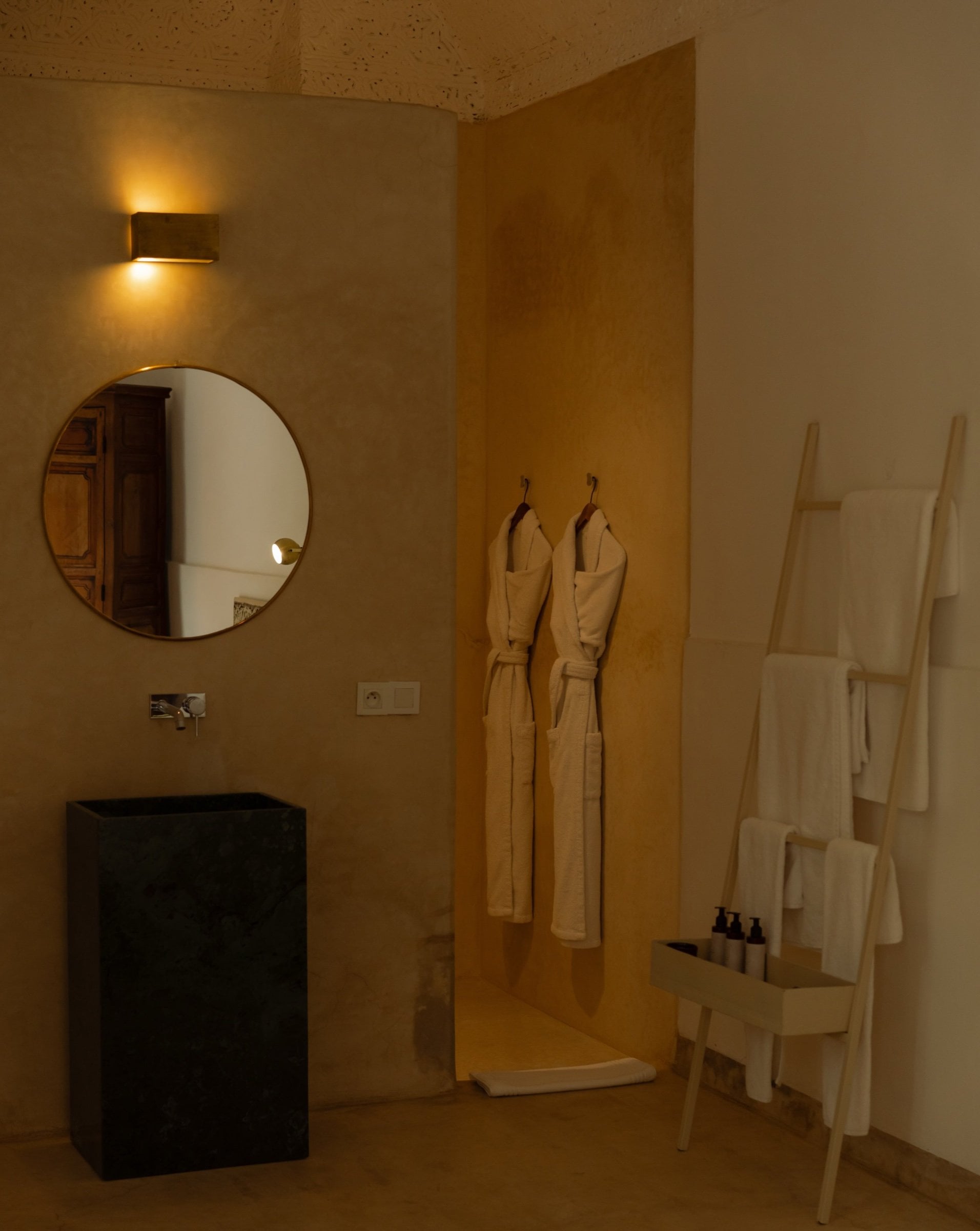 Bathroom at Numa Marrakech with a round mirror, a stone washbasin, bathrobes and a towel ladder