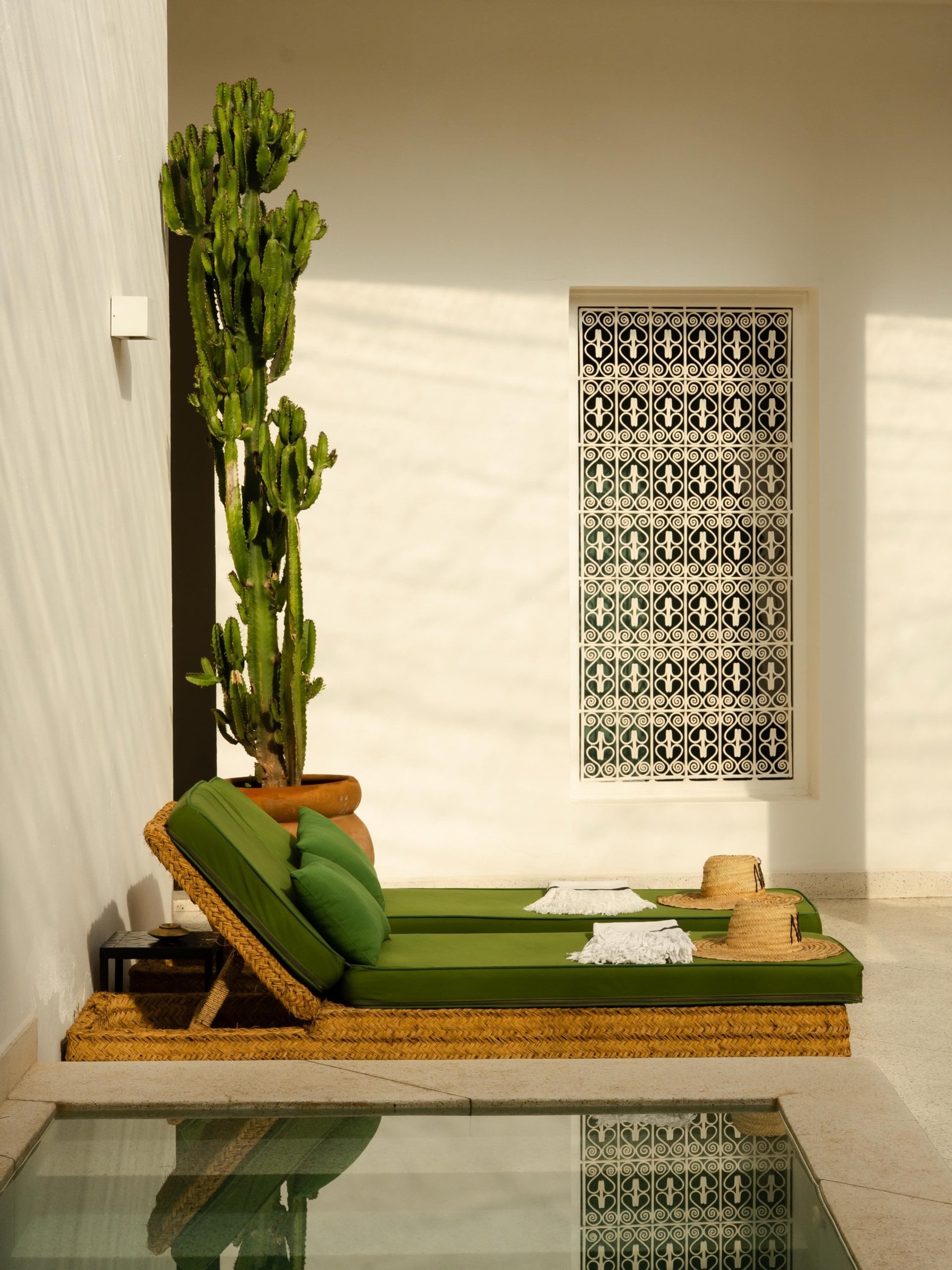 Green sun loungers and a tall cactus beside the pool at Numa Marrakech, under a carved white screen