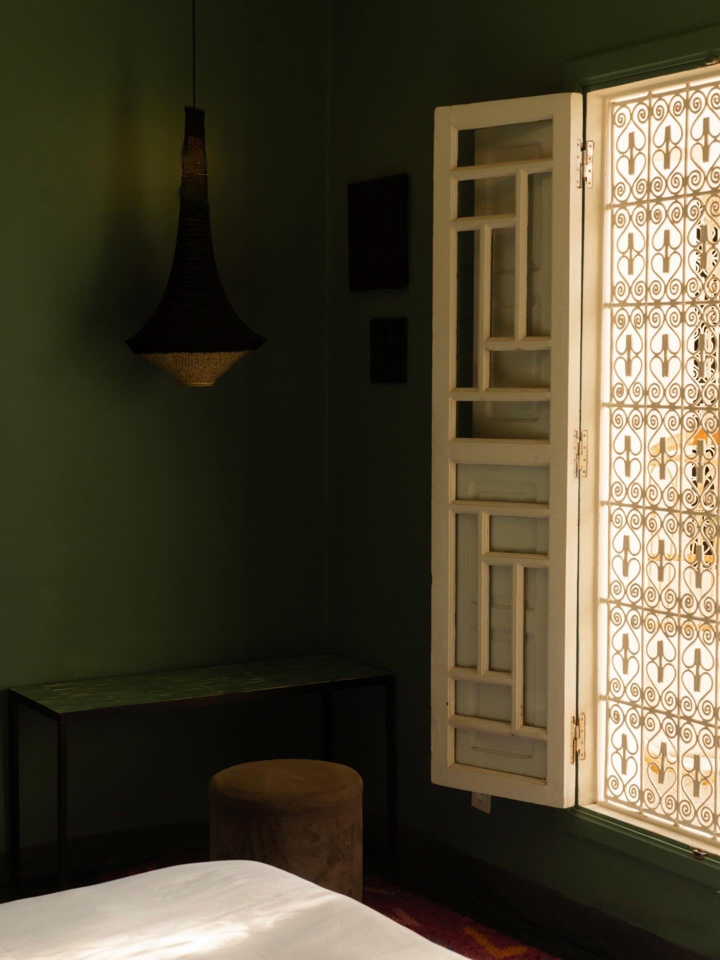 Dark green room at Numa Marrakech with a woven pendant lamp and an open carved wooden window