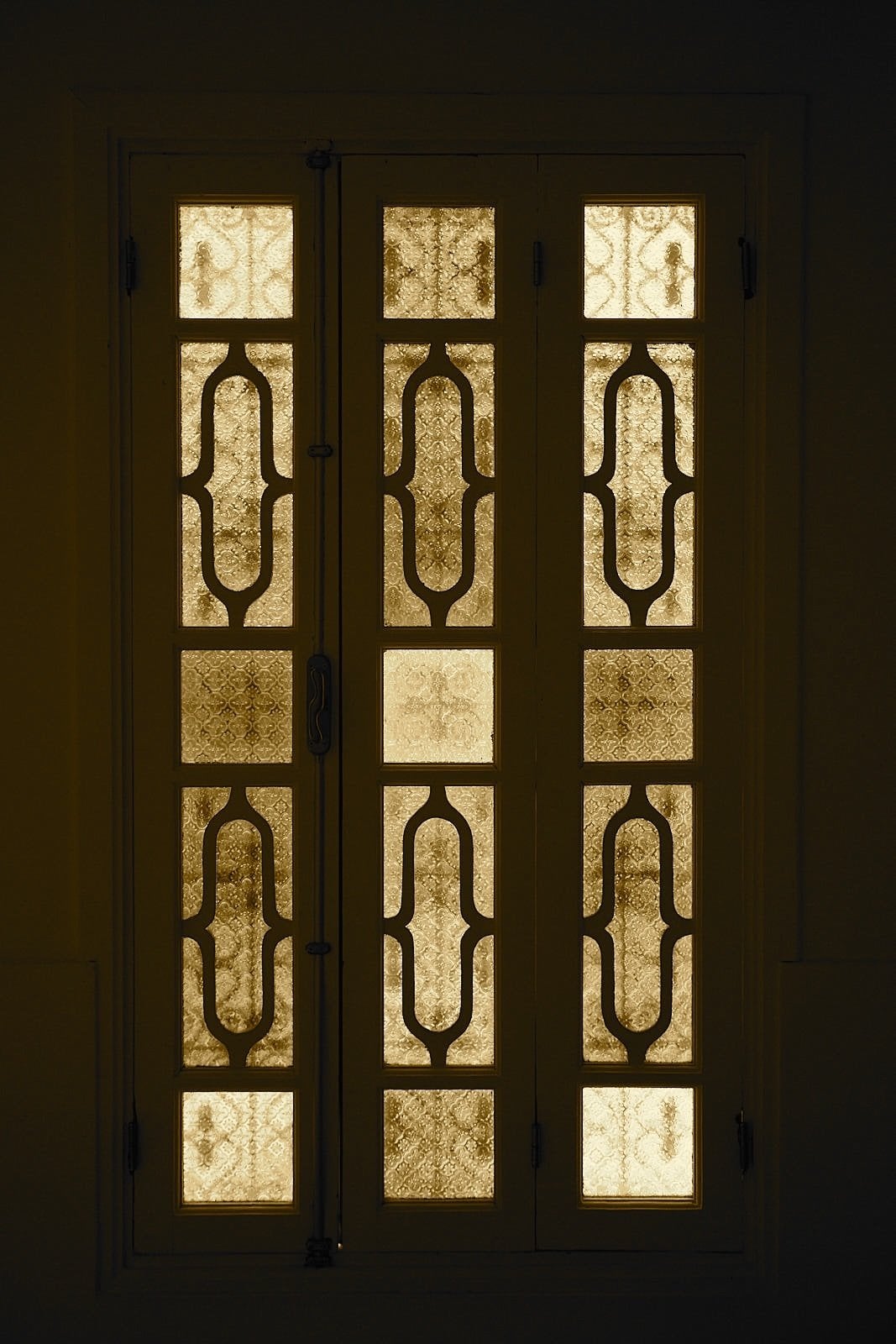 Wooden window with patterned amber glass panes glowing in the dark at Numa Marrakech