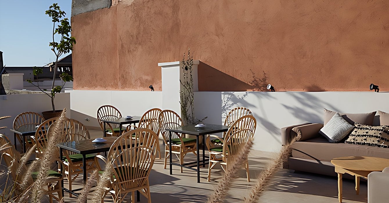 Rooftop terrace of Numa Marrakech with rattan chairs, small tables and a sofa against a terracotta wall