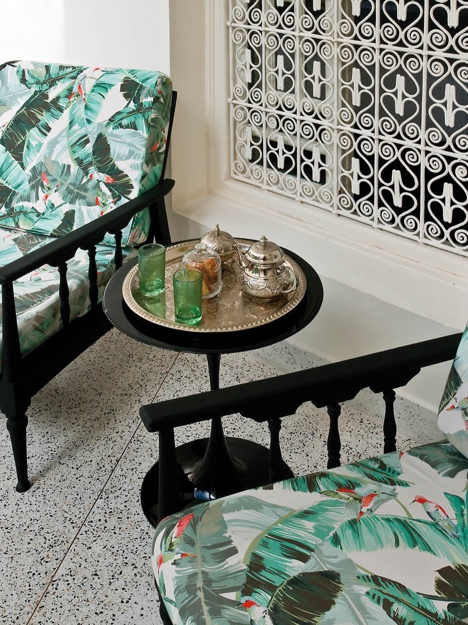 Silver tea tray with green glasses between leaf-print armchairs by a lattice railing at Numa Marrakech