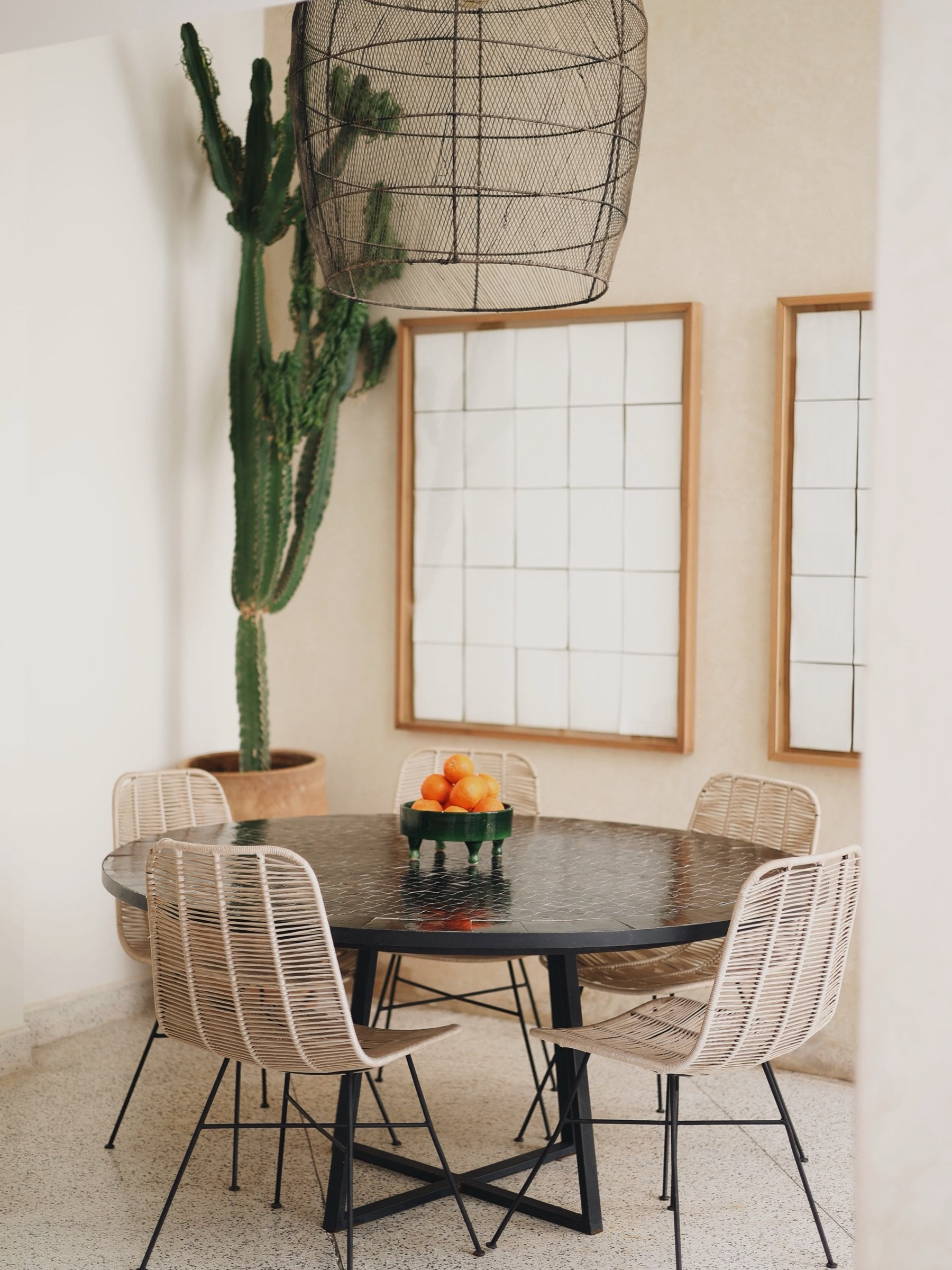 Round table with rattan chairs, a bowl of oranges and a tall cactus at Numa Marrakech