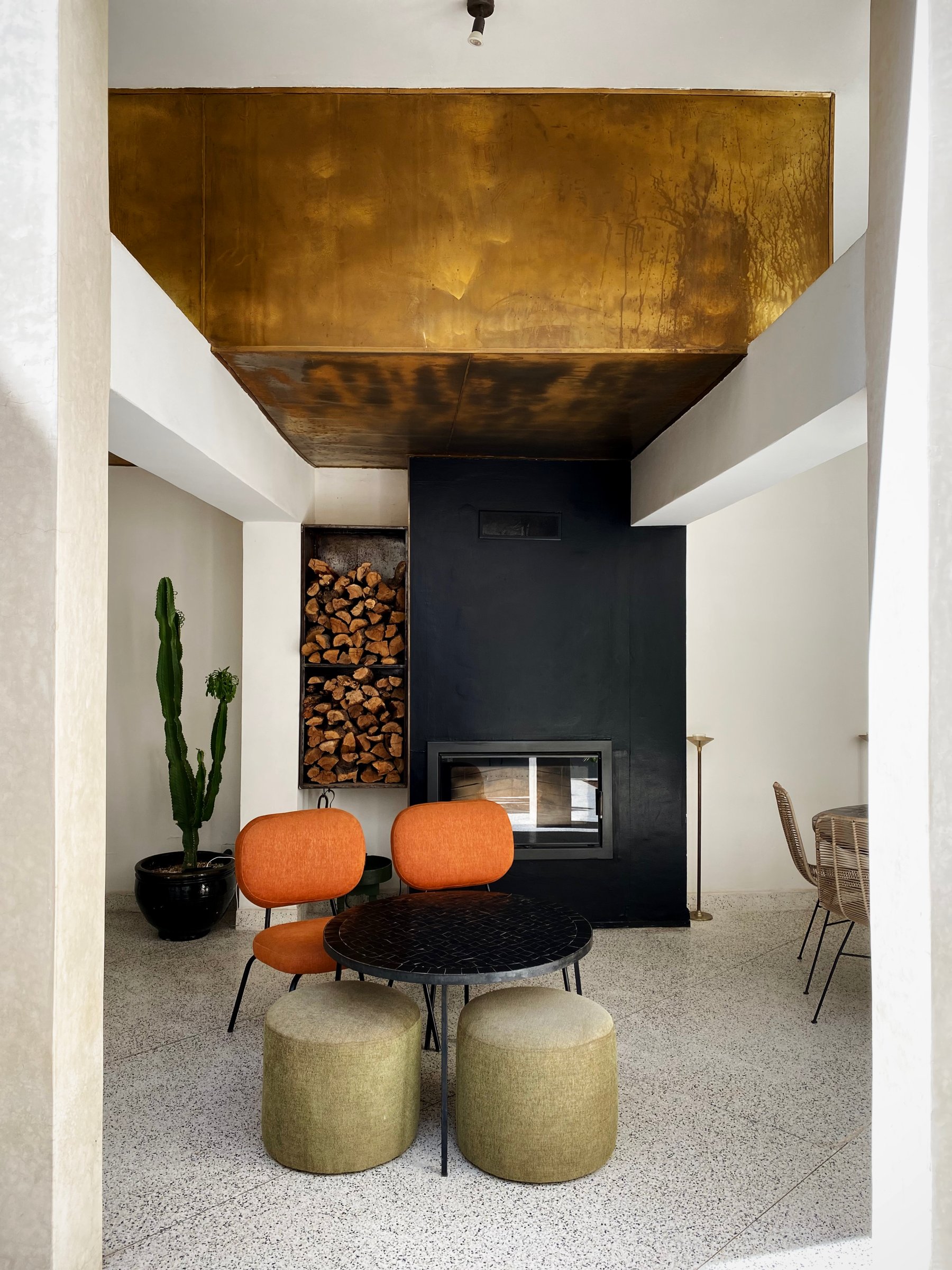 The living area at Numa, with orange chairs around a table and a black fireplace under a gilded ceiling