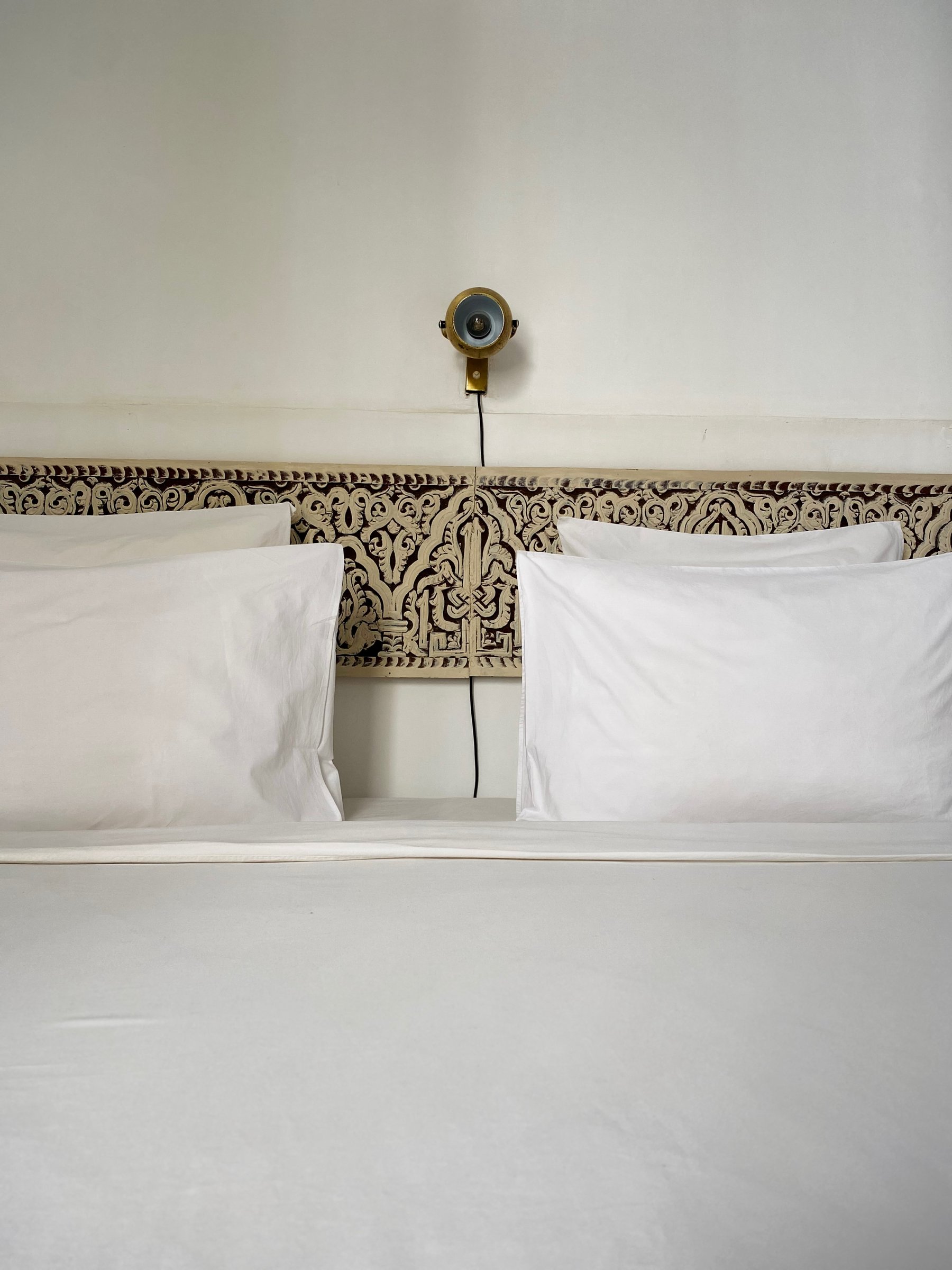 A carved wooden headboard and a brass reading lamp above white pillows at Numa