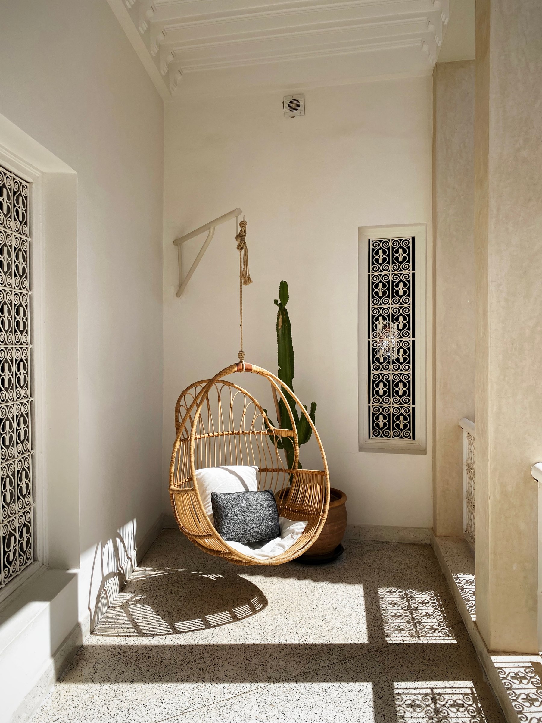 A hanging rattan chair in a sunny corner of Numa, between carved wooden screens
