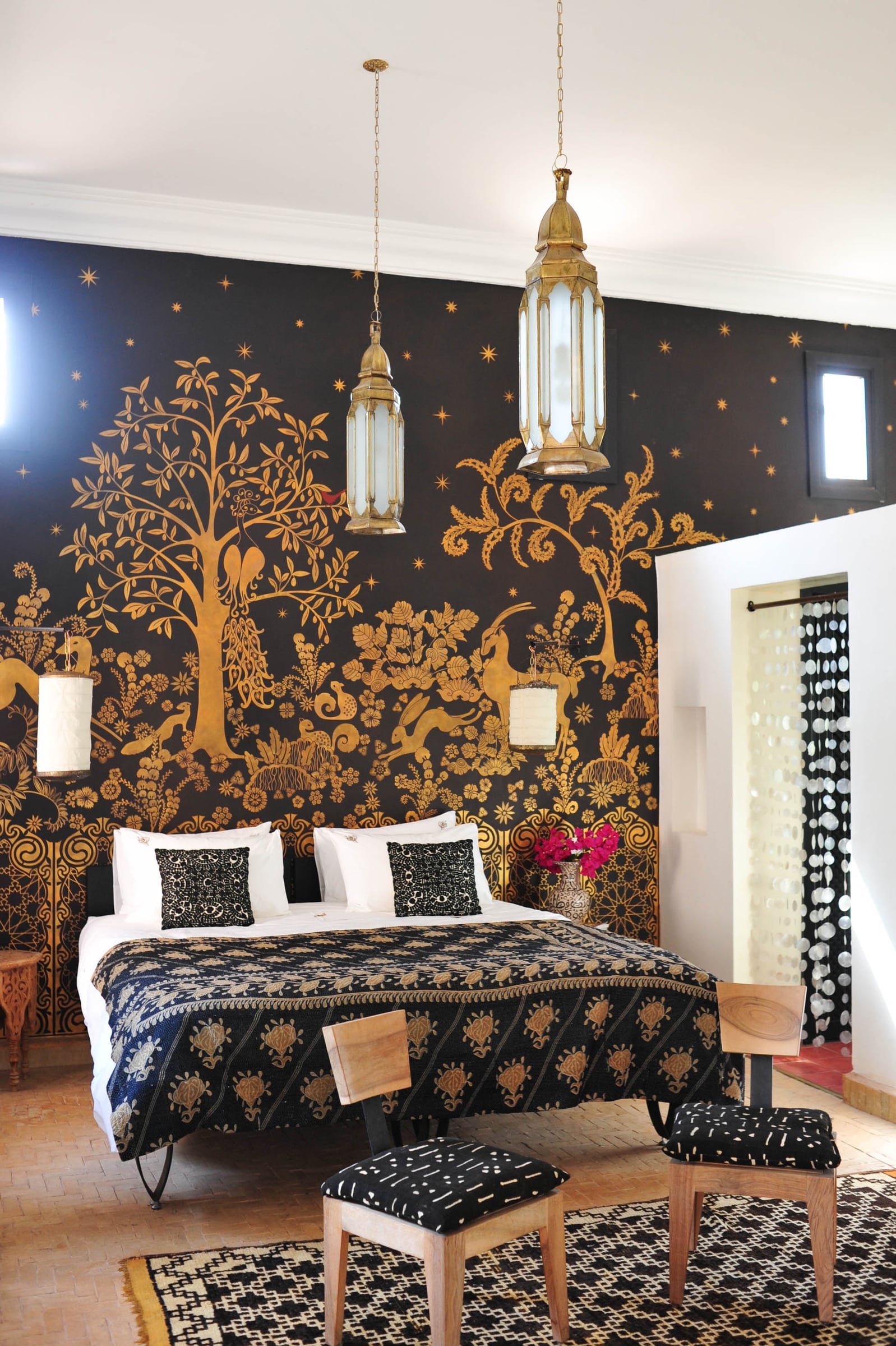 Golden Gazelle Room: hand-painted gold tree-of-life mural on a black wall, two brass lanterns hanging low over the bed.