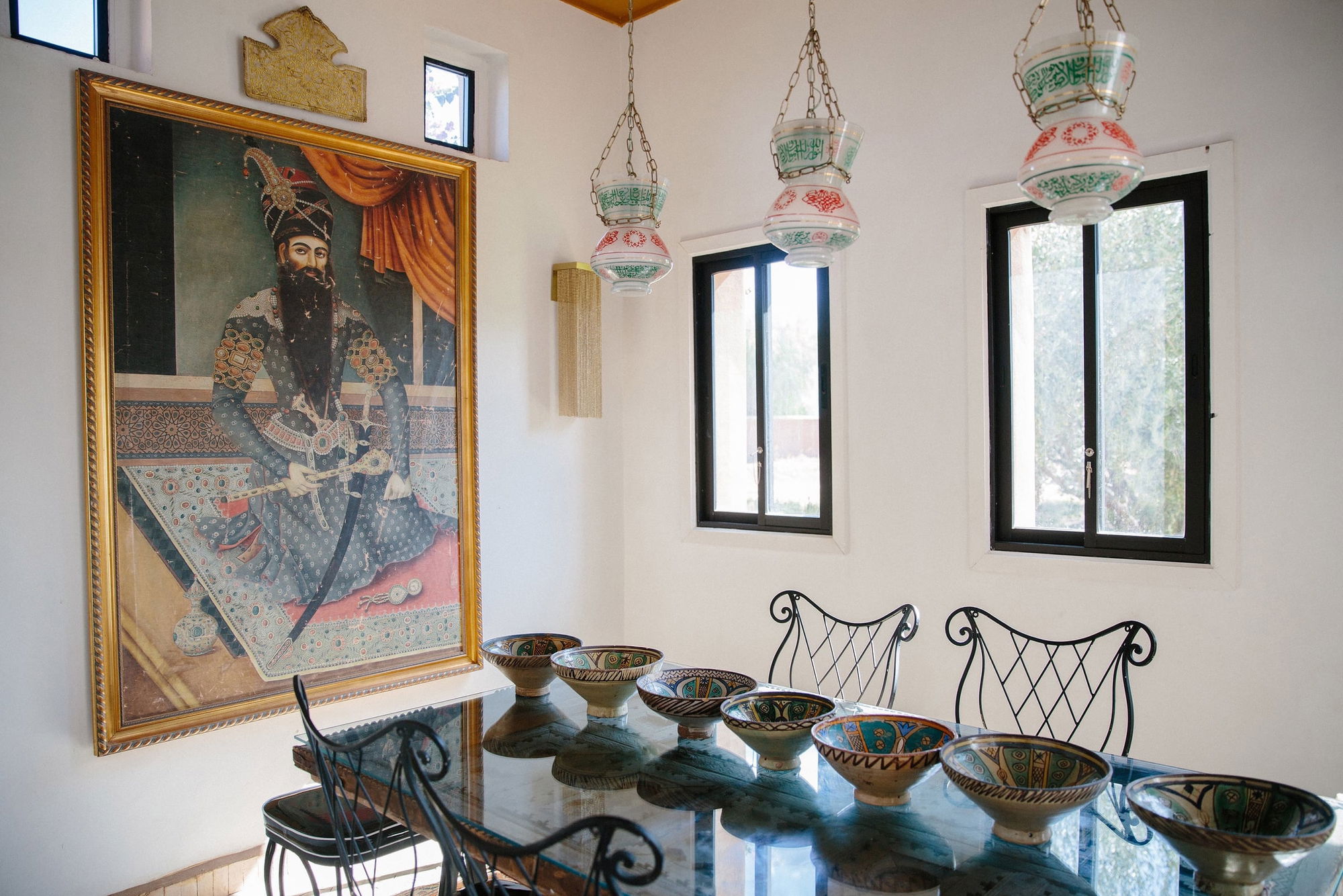 Medina Pavilion dining nook under hanging glass lanterns painted with Arabic script, below a large framed portrait.