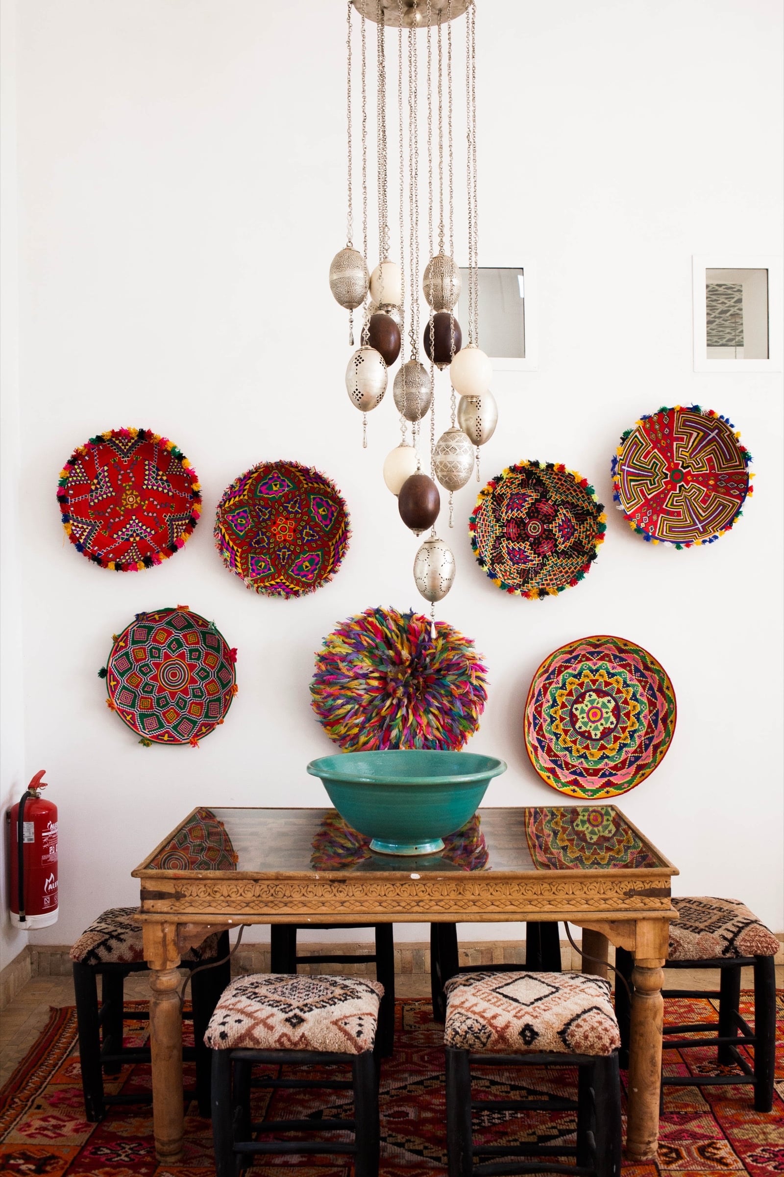 Atlas Pavilion dining area: wall hung with round woven and beaded plates under a silver and dark-wood bead chandelier.