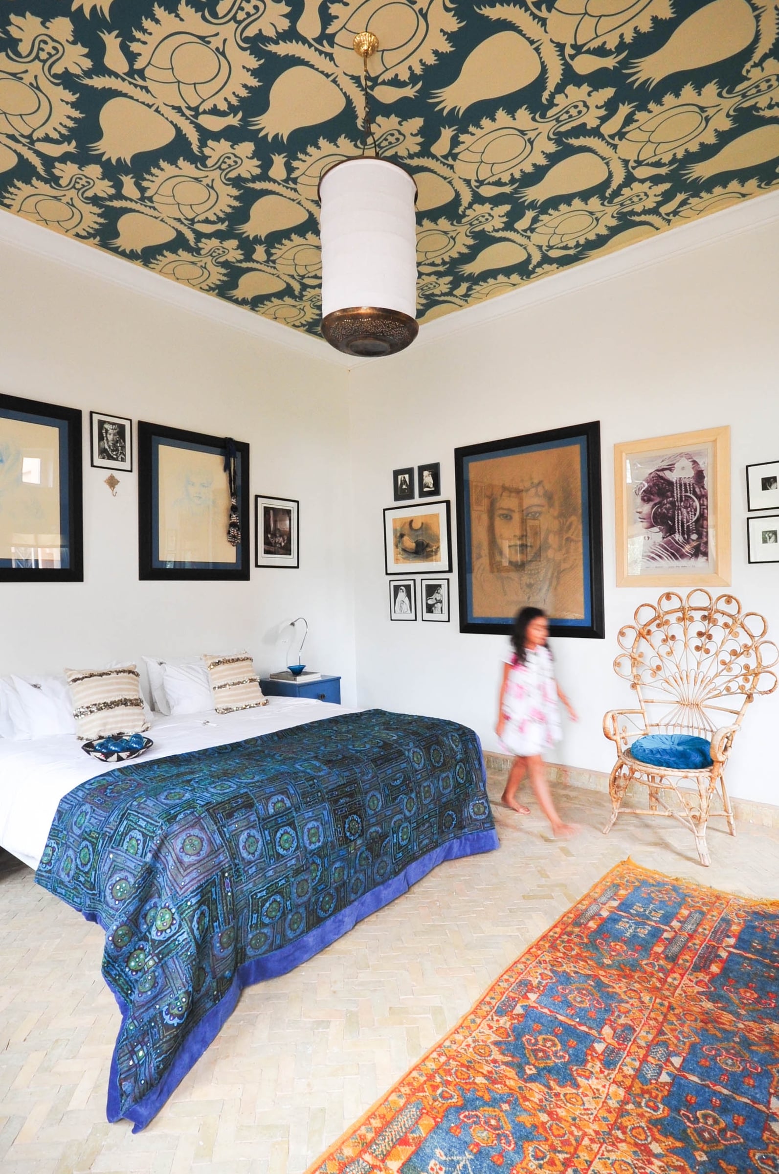 Moorish Muse Room with a gold bird-and-leaf ceiling mural on a dark teal ground and a wicker peacock chair.