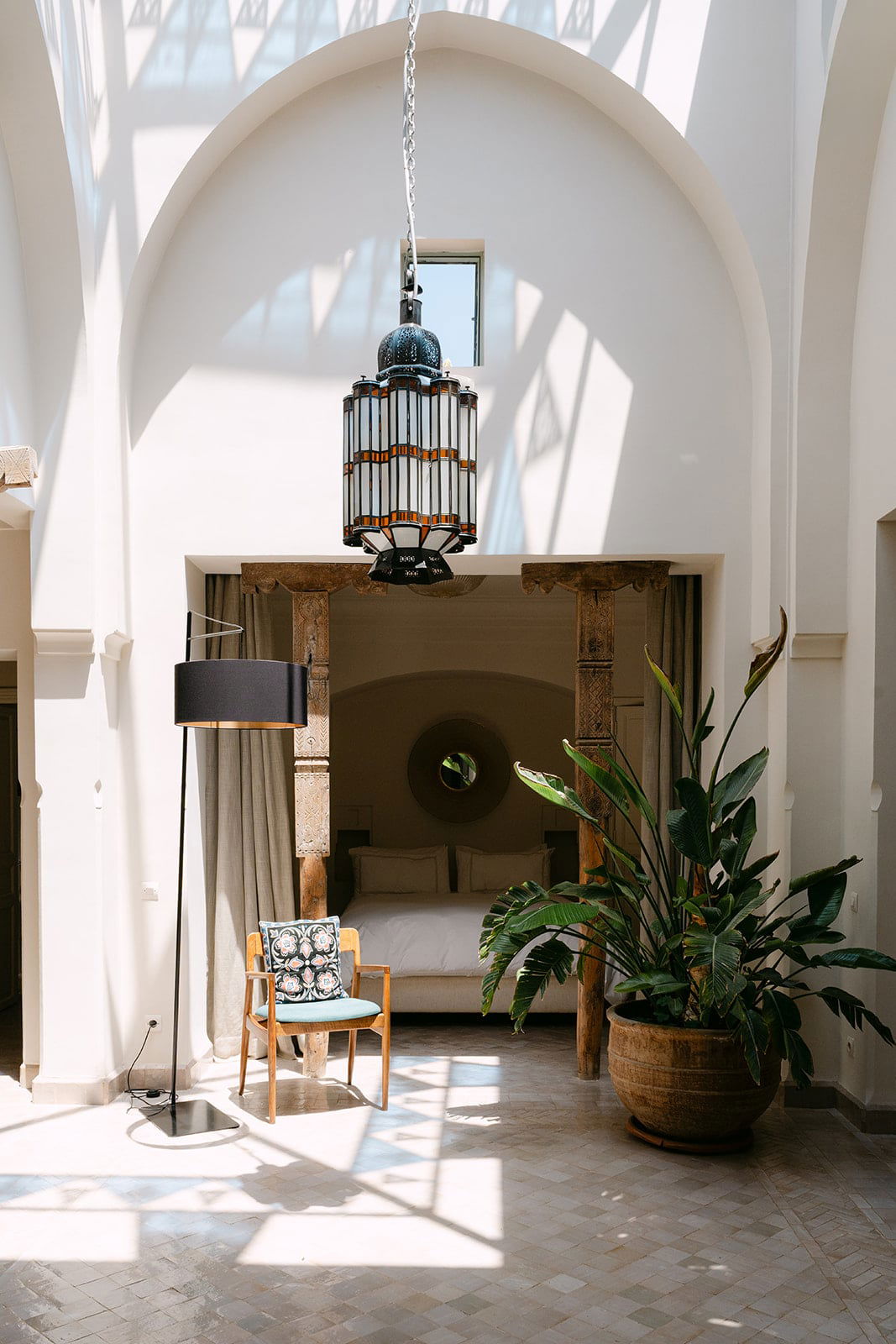Carved wooden posts frame the alcove bed, a round mirror behind and a Moroccan stained-glass lantern above.