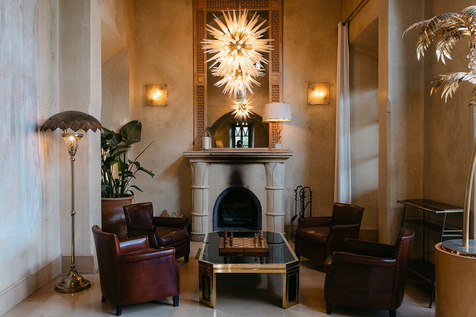 Fireside lounge with a spiked glass starburst chandelier, brown leather club chairs and a chess set on a brass table.