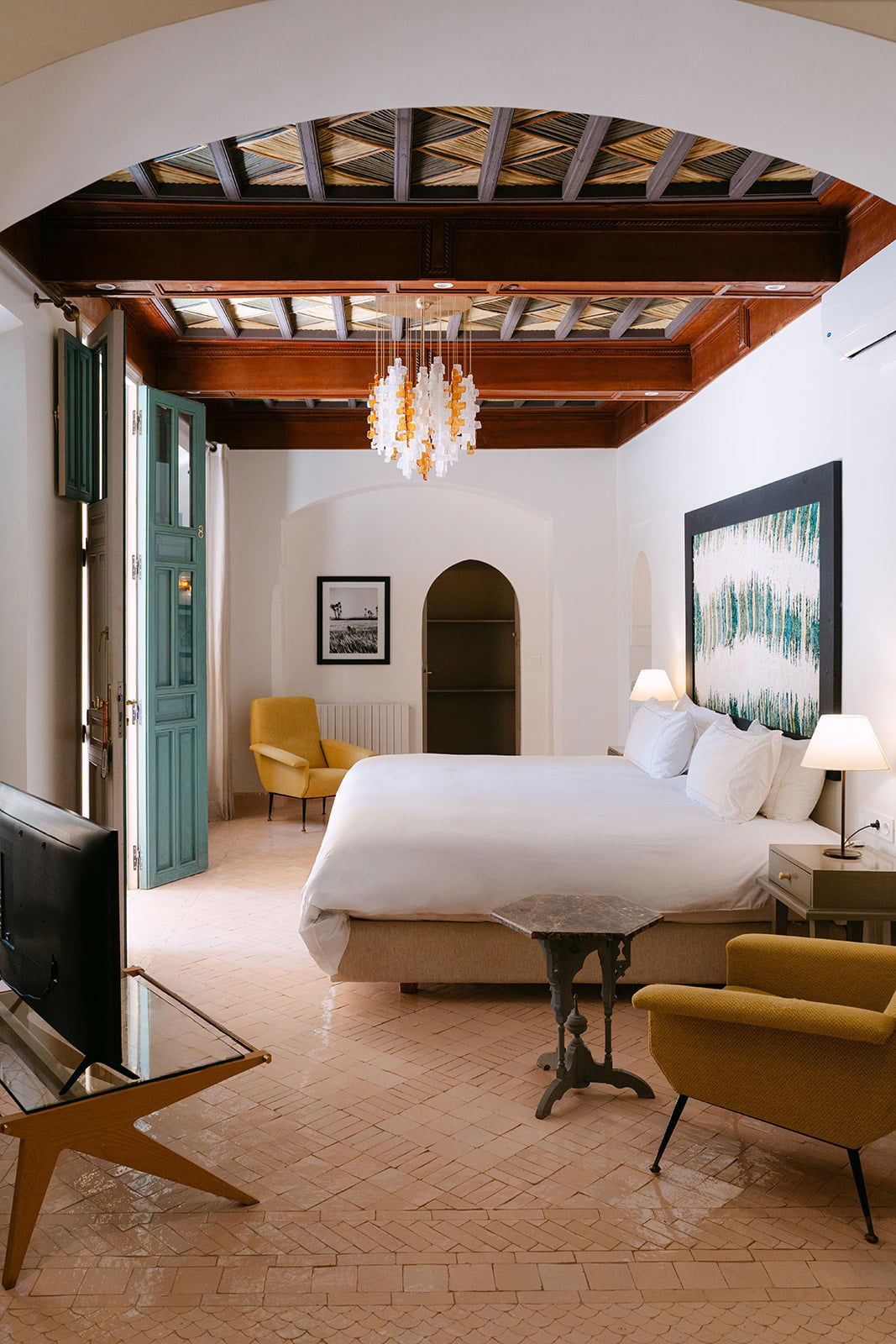 Bedroom with mustard velvet armchairs, a terracotta herringbone floor and a reed-and-beam ceiling laid in chevron.