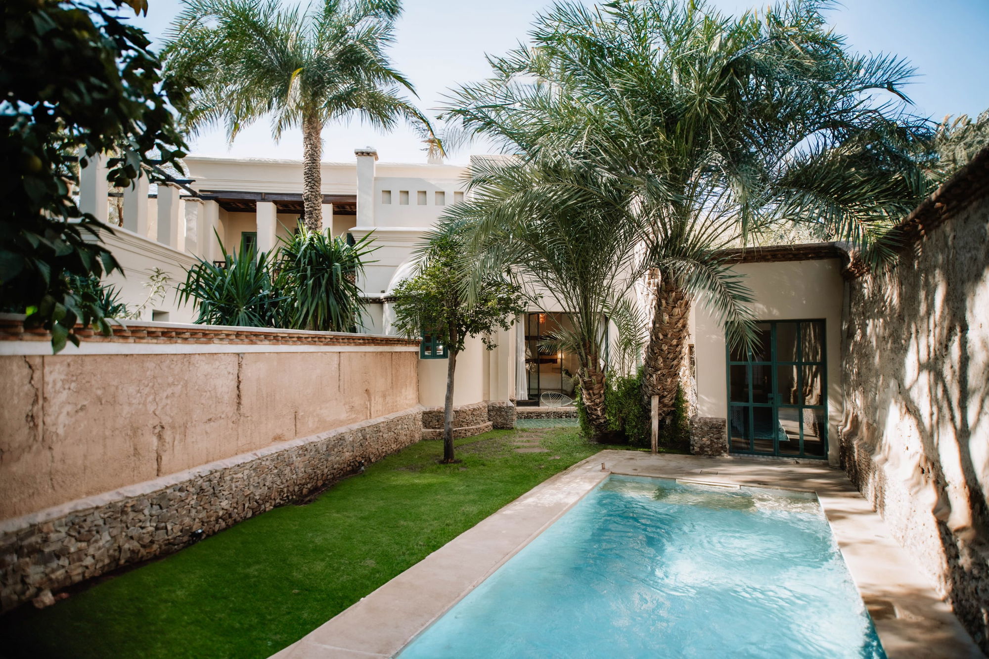 A Pool Suite's walled garden: a long private pool, lawn, date palms and the suite's teal glazed doors.