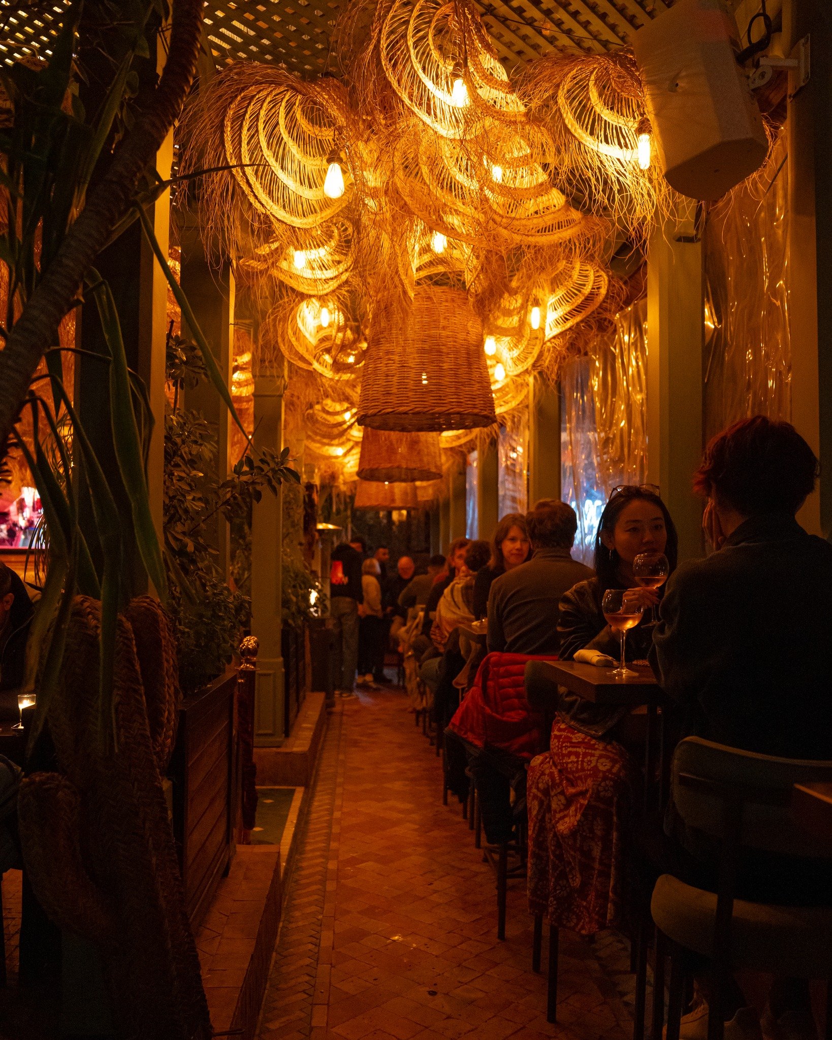 A passage at La Pergola lit by woven lamps at night, diners along the tables