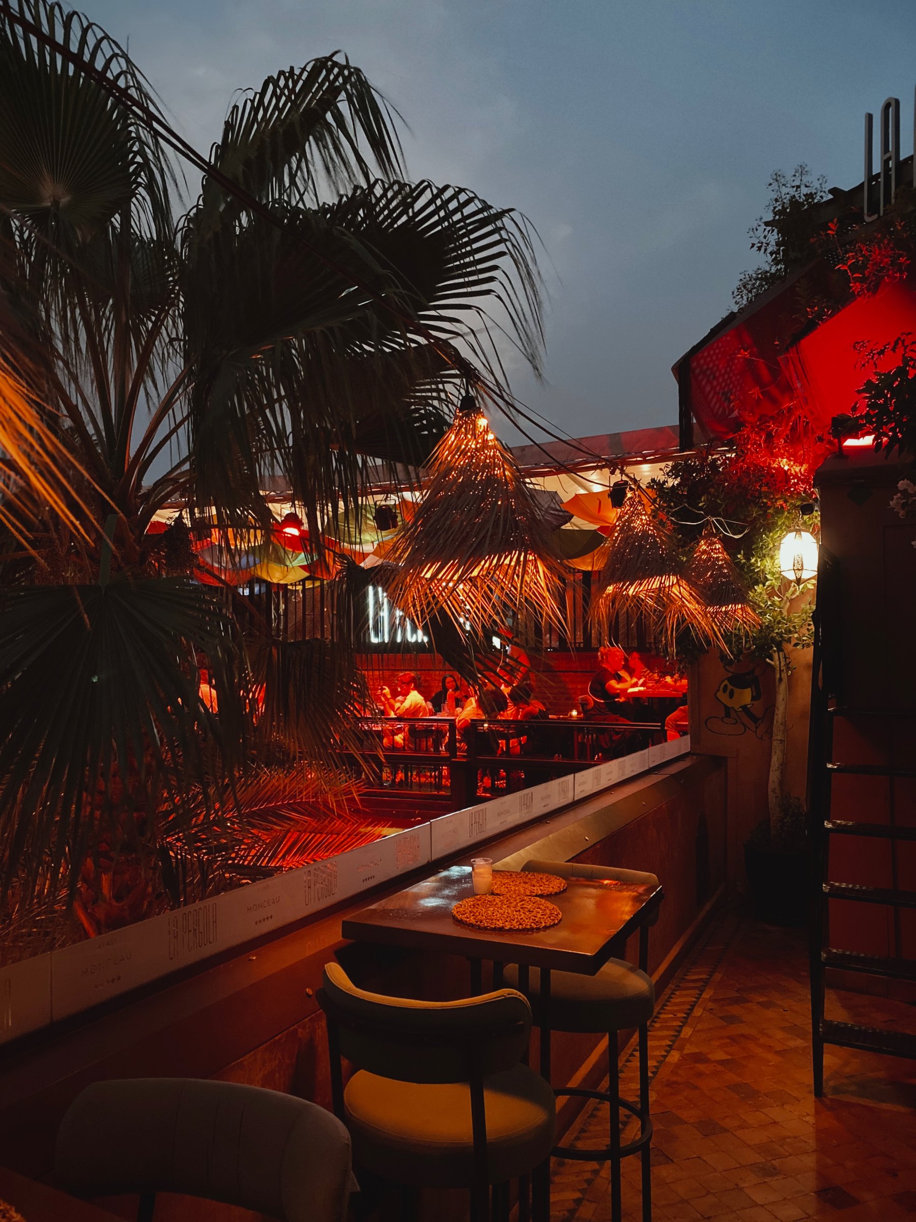 A table on the La Pergola terrace at dusk, with straw lamps and palms behind