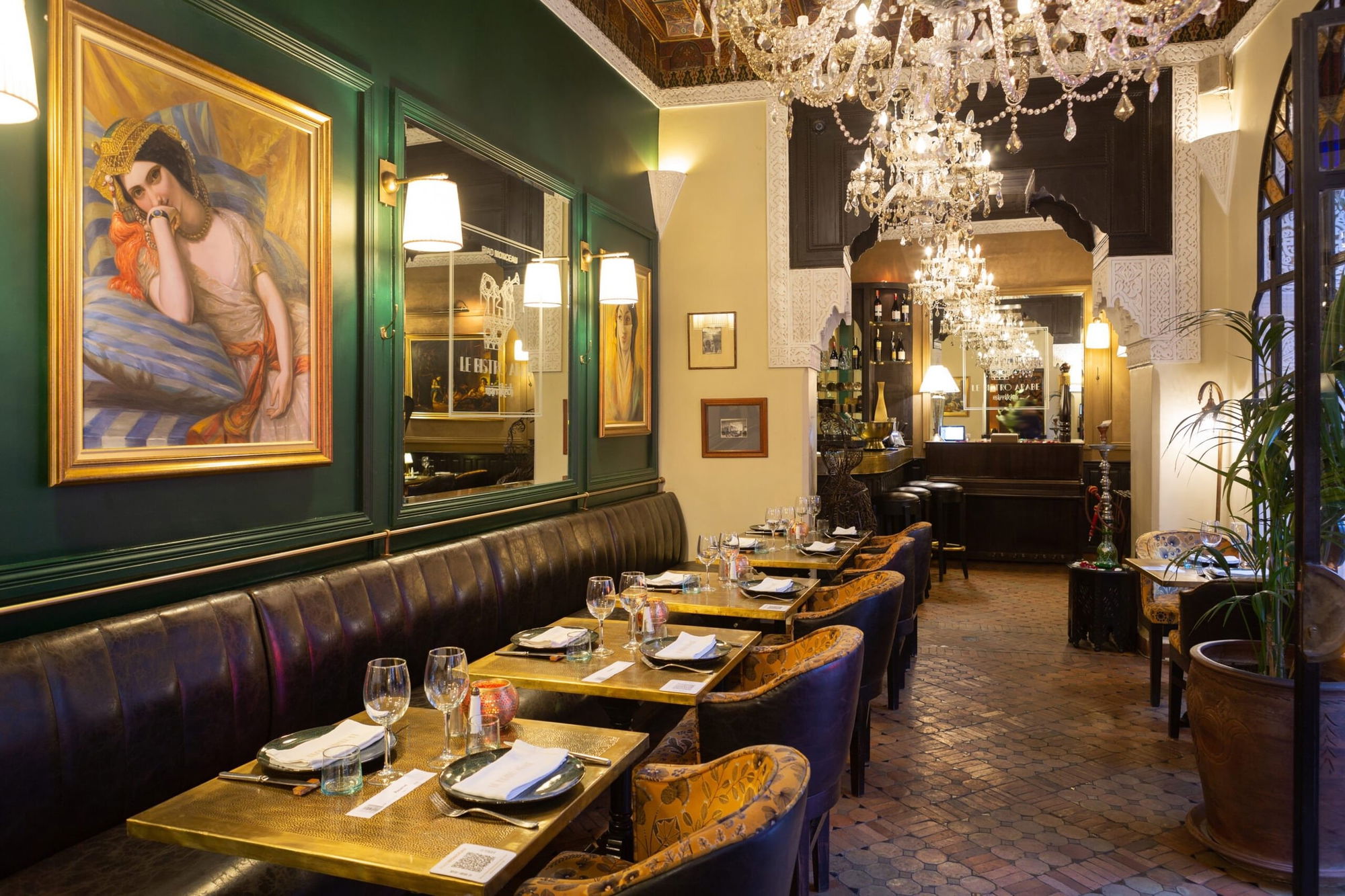 Main dining room of Le Bistro Arabe with green walls, crystal chandeliers, leather banquettes and the orientalist portrait