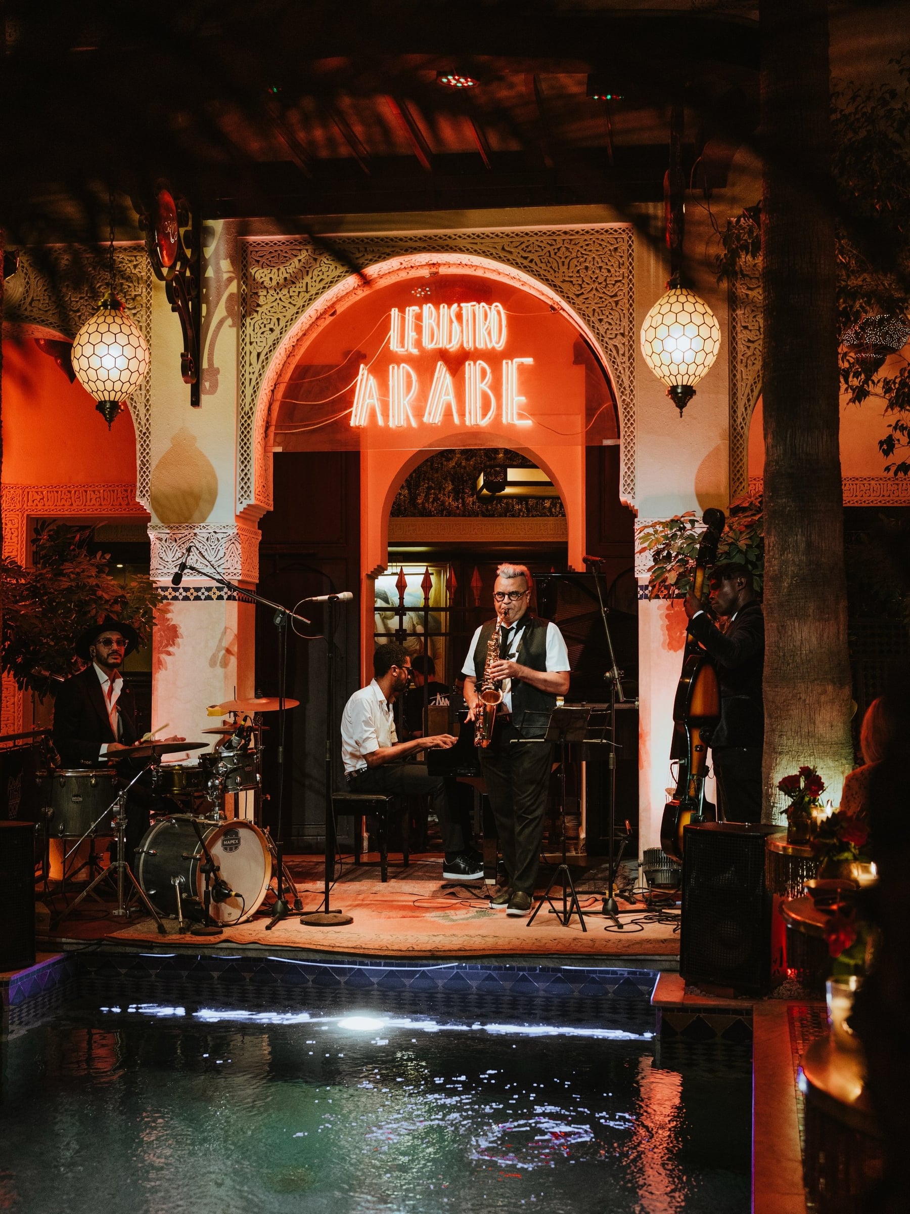Jazz band playing under the red neon Le Bistro Arabe sign, the stage set above the courtyard pool