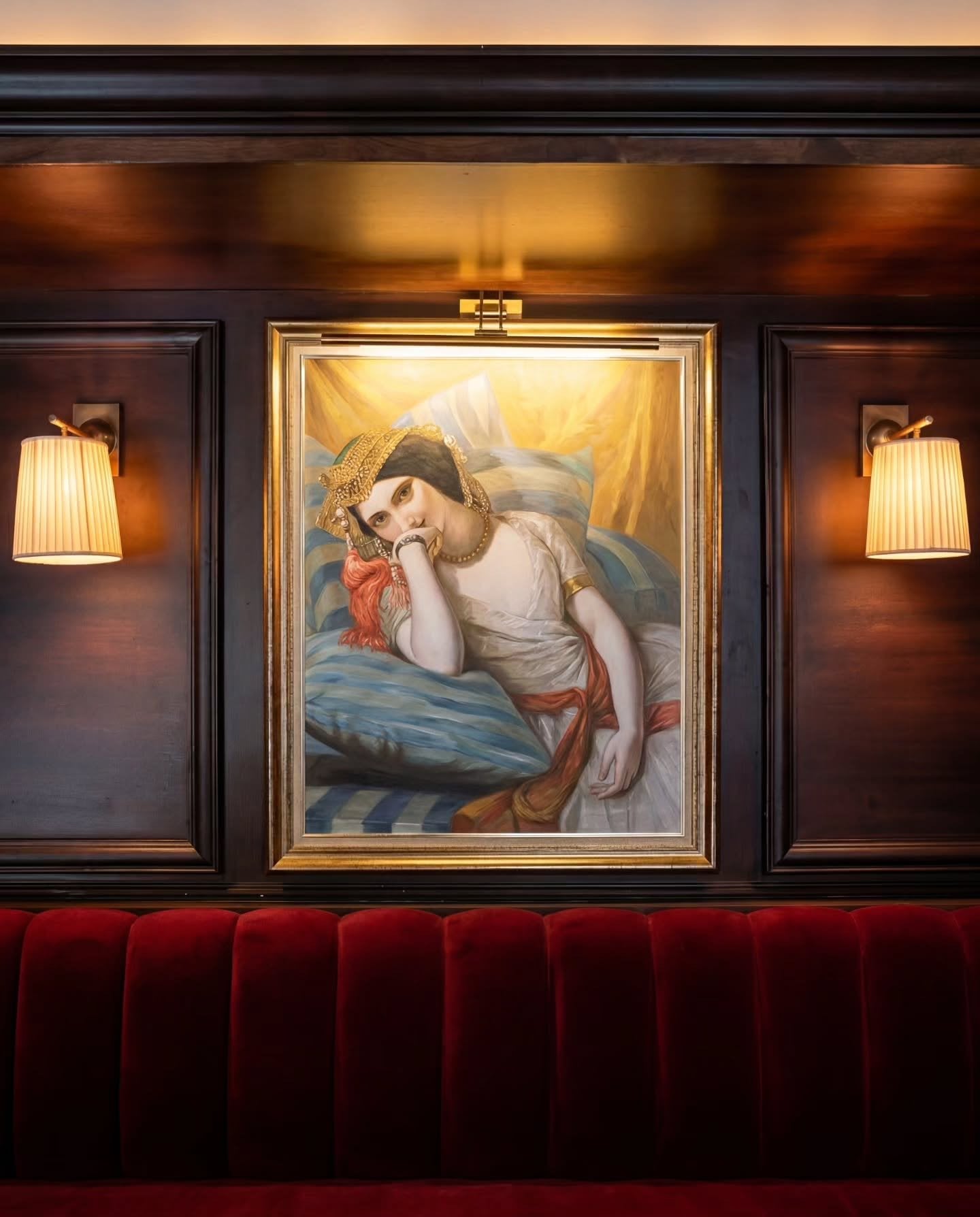 The orientalist portrait of a reclining woman at Le Bistro Arabe, lit above a red velvet banquette