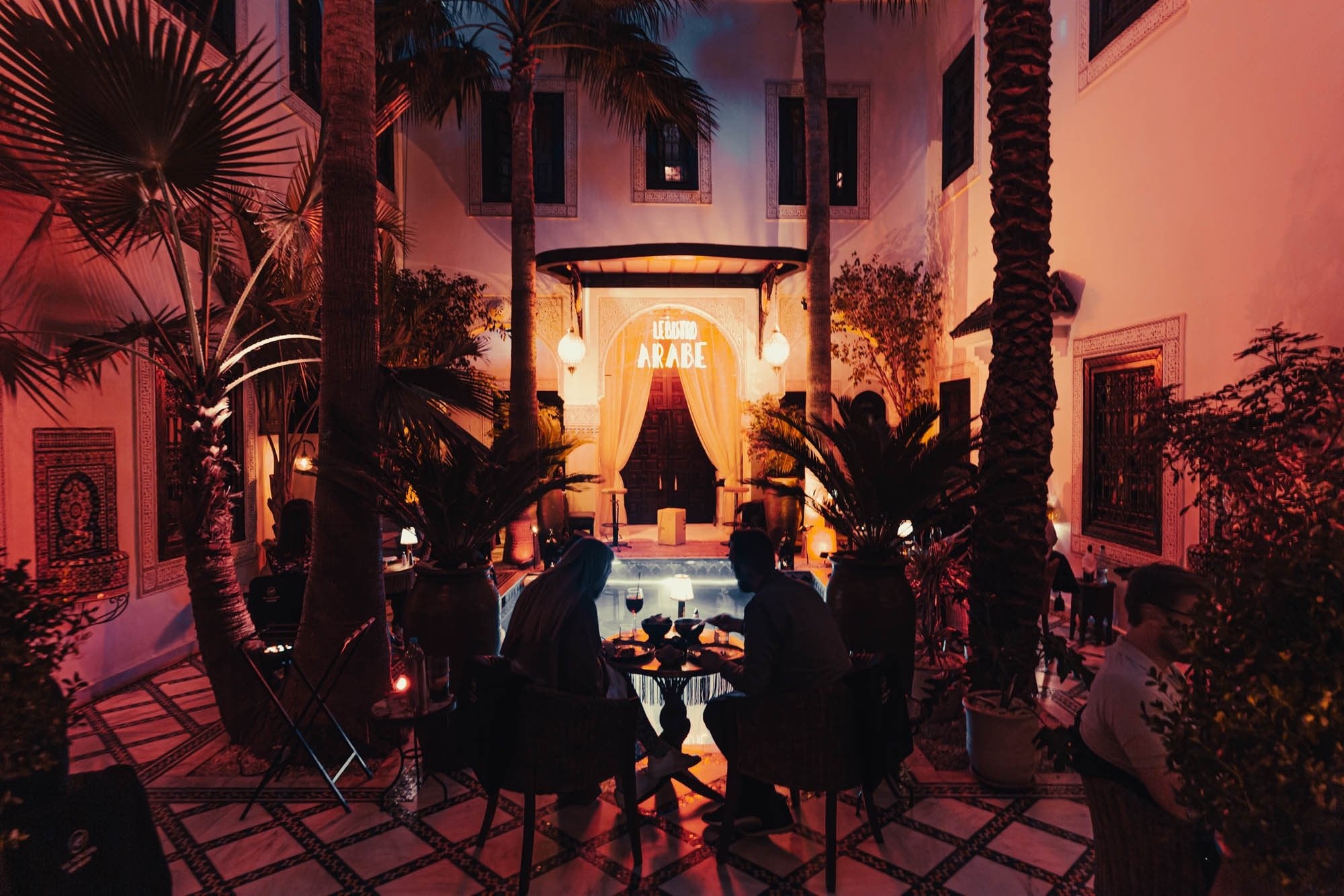 The courtyard of Le Bistro Arabe at night, diners among palms facing the arch with the restaurant's sign
