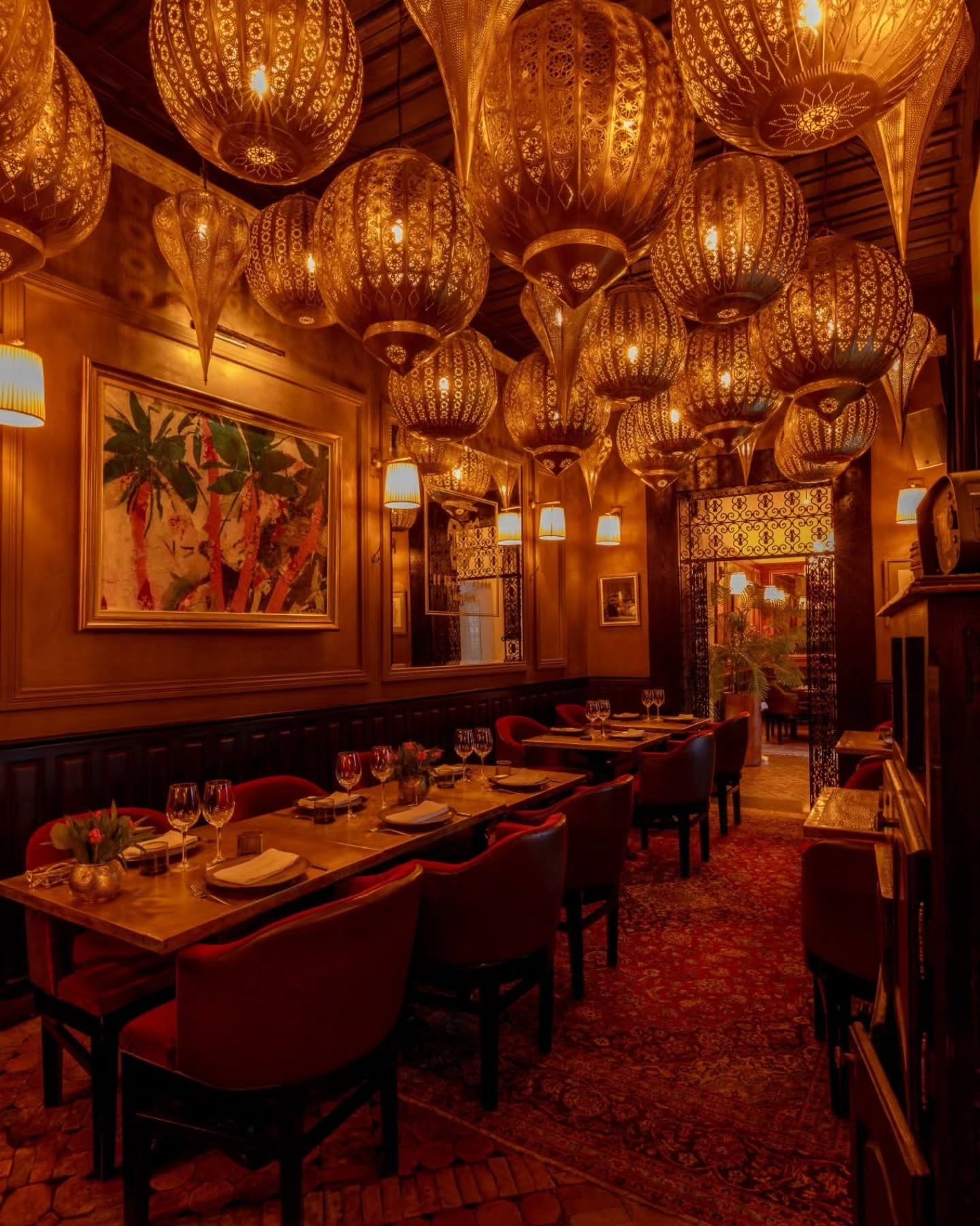 A dining room at Le Bistro Arabe under dozens of pierced brass lanterns, with red chairs and paintings