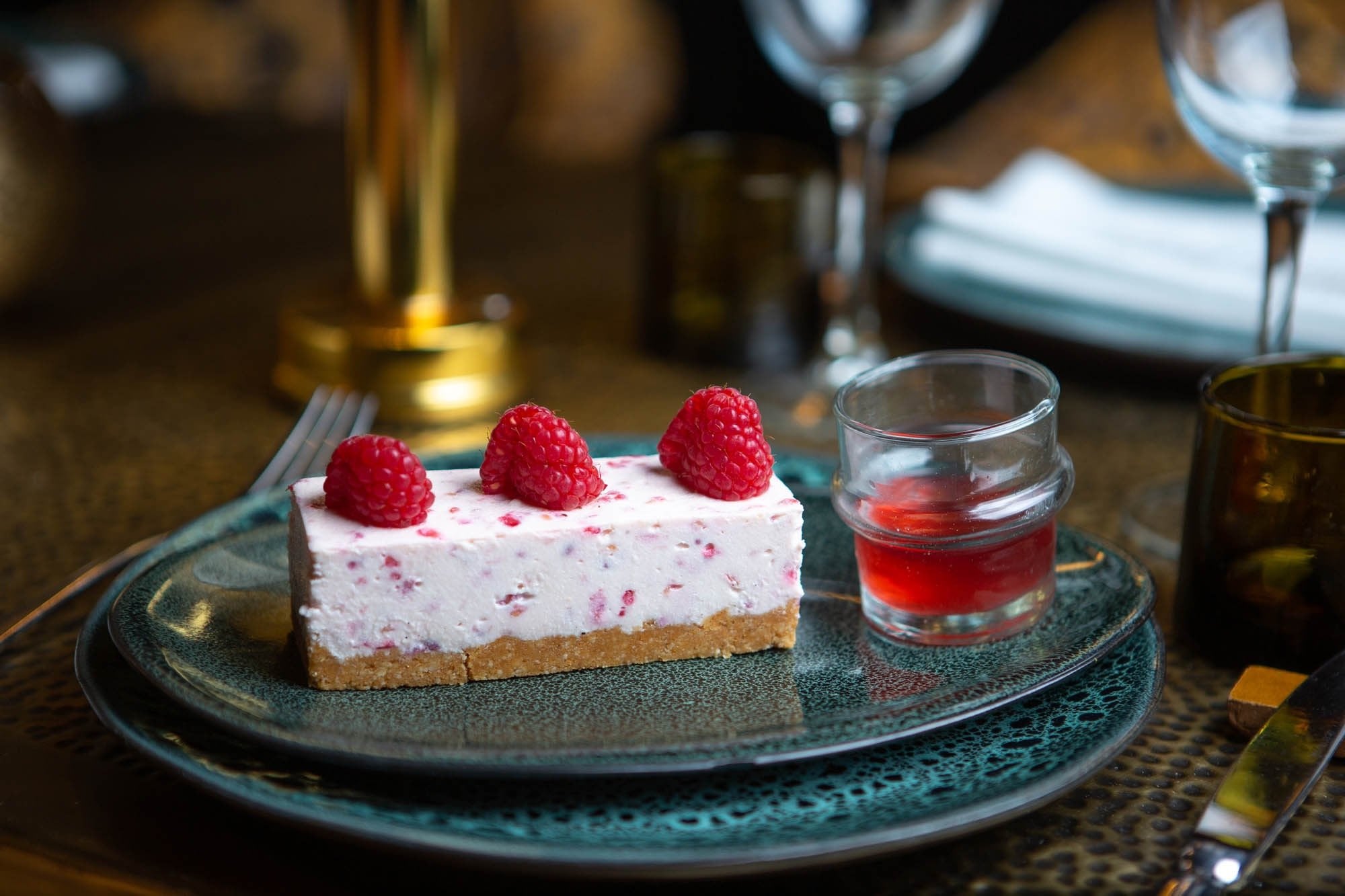 Raspberry cheesecake with a small glass of red sauce on a green plate at Le Bistro Arabe