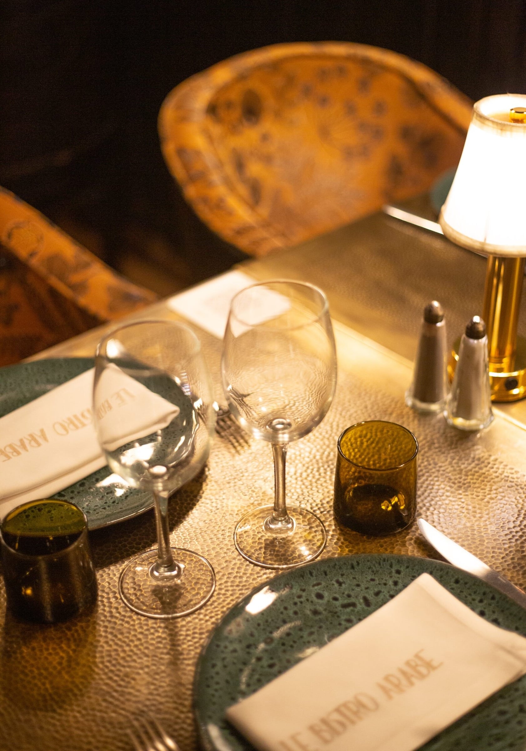 Table laid at Le Bistro Arabe with wine glasses, a brass lamp and a napkin printed with the restaurant's name