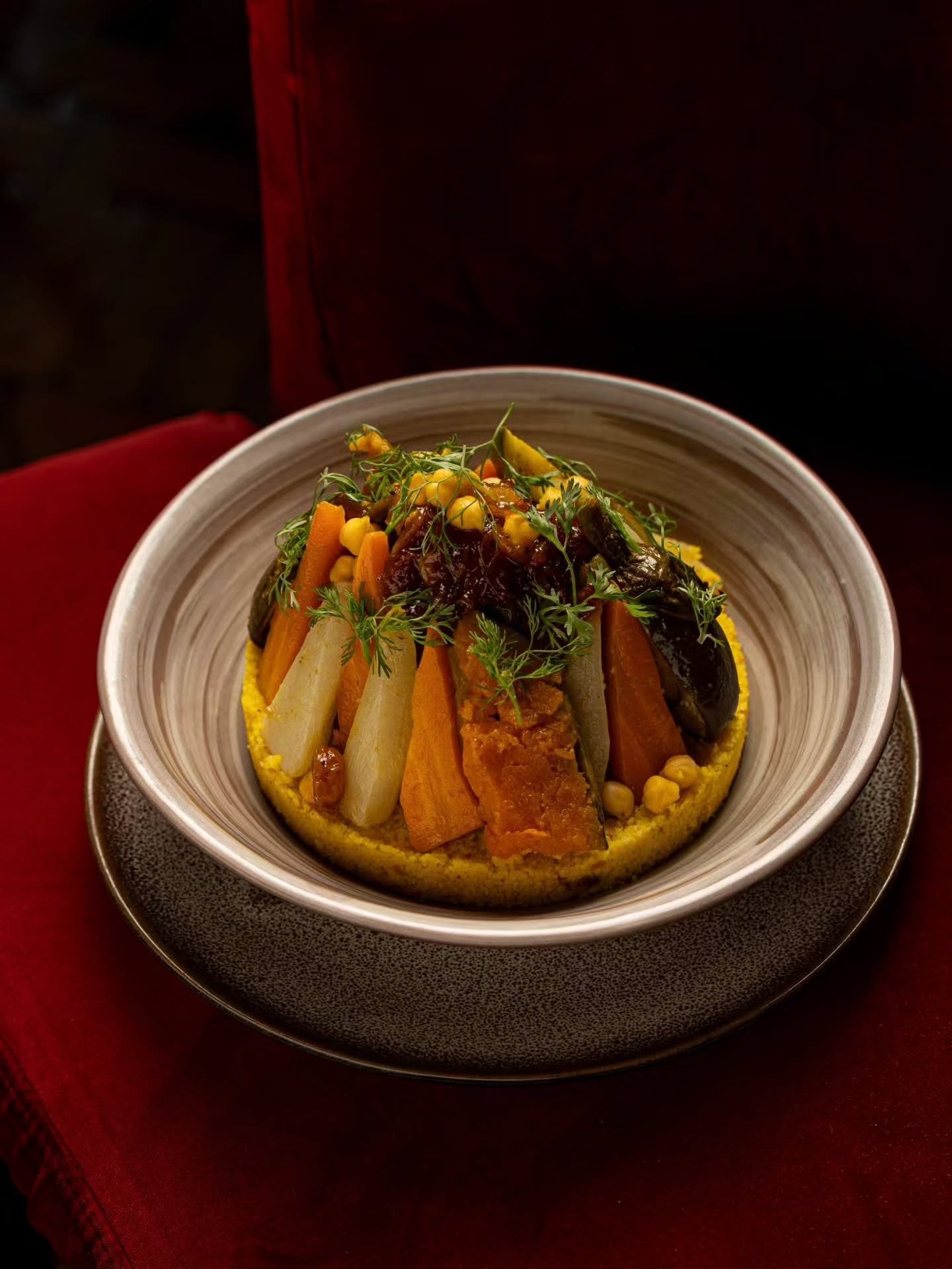Couscous topped with vegetables, chickpeas and herbs in a deep bowl at Le Bistro Arabe