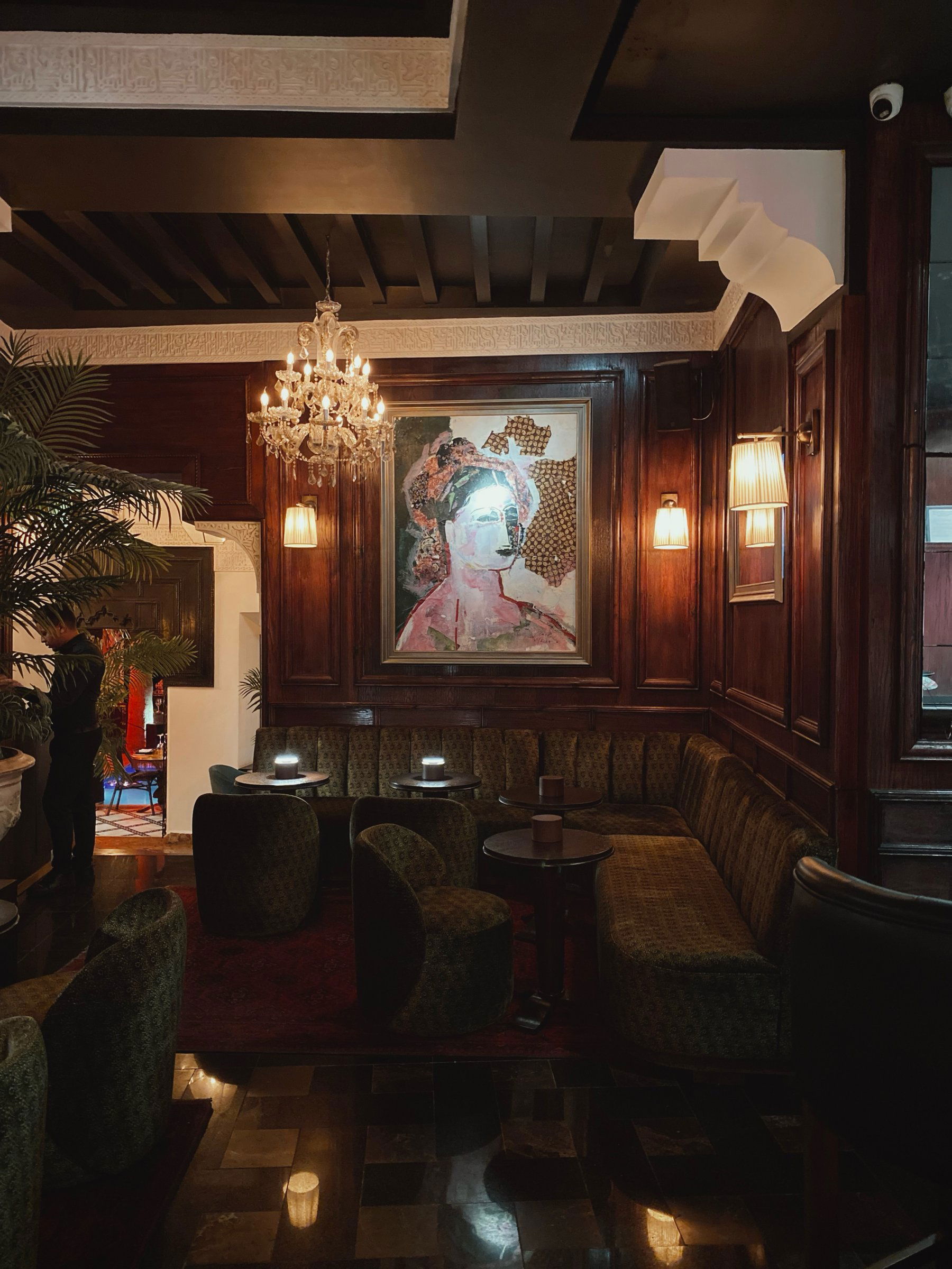 A lounge corner with green velvet banquettes, a crystal chandelier and a portrait painting