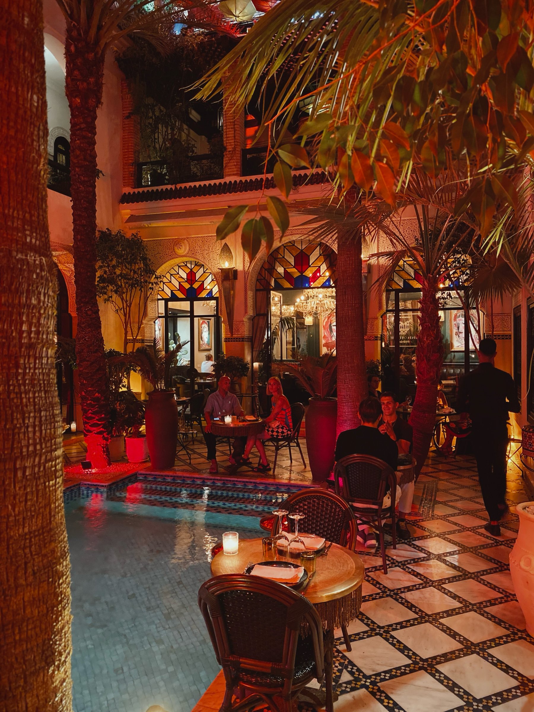 The riad courtyard at night, with tables set around the pool under the palms
