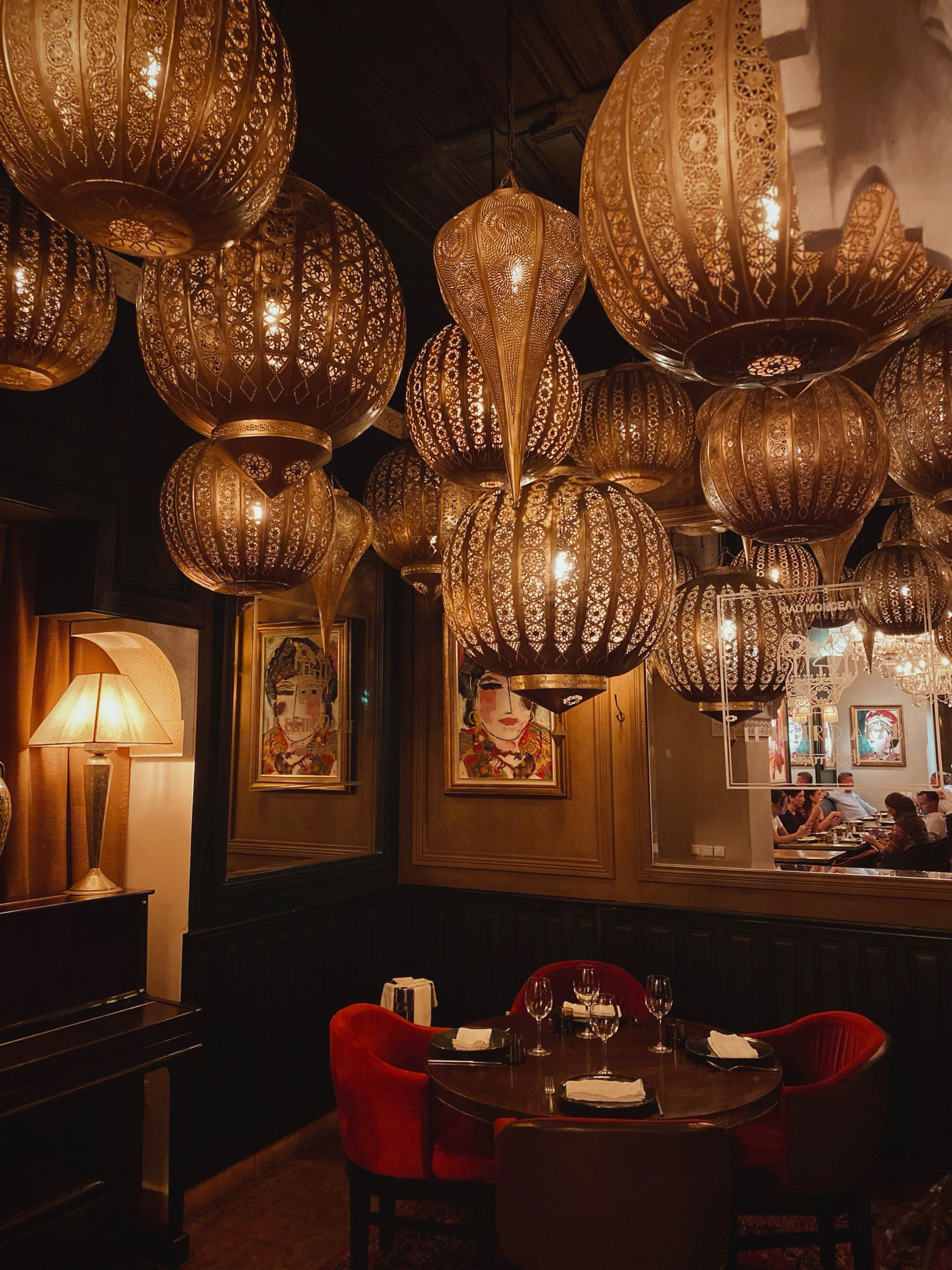 Brass lanterns hanging over a table with red velvet chairs and portrait paintings