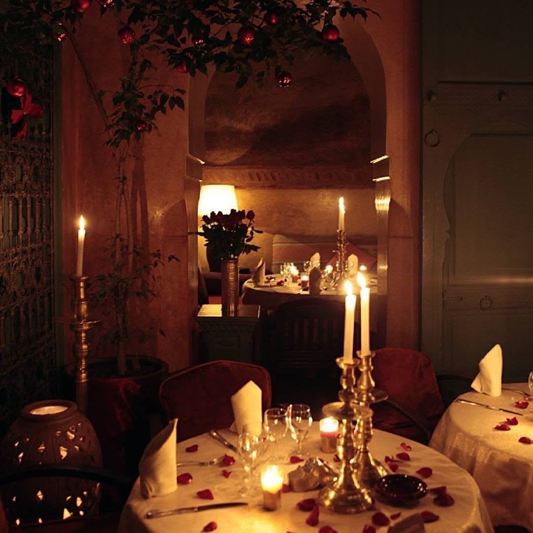A table at Le Tobsil set with brass candlesticks, candles and rose petals, with a vase of roses behind