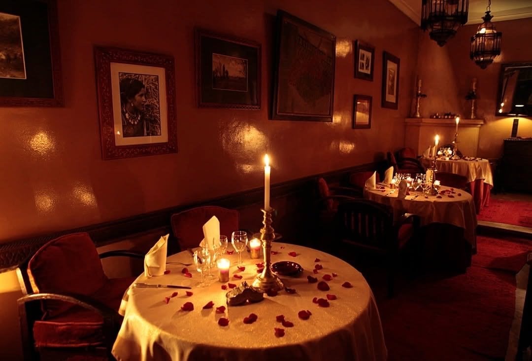 A dining salon at Le Tobsil with framed photographs on the walls and candlelit tables strewn with rose petals