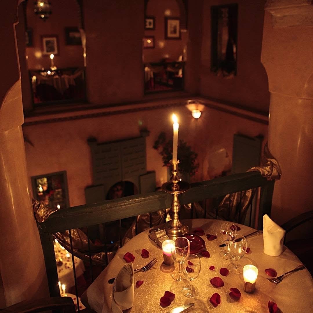 A table on the gallery of Le Tobsil with a brass candlestick and rose petals, overlooking the courtyard