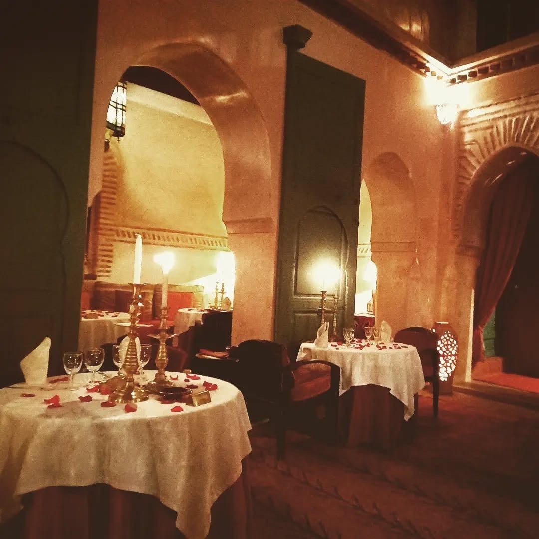 Candlelit tables with brass candelabra under the arches of a dining room at Le Tobsil