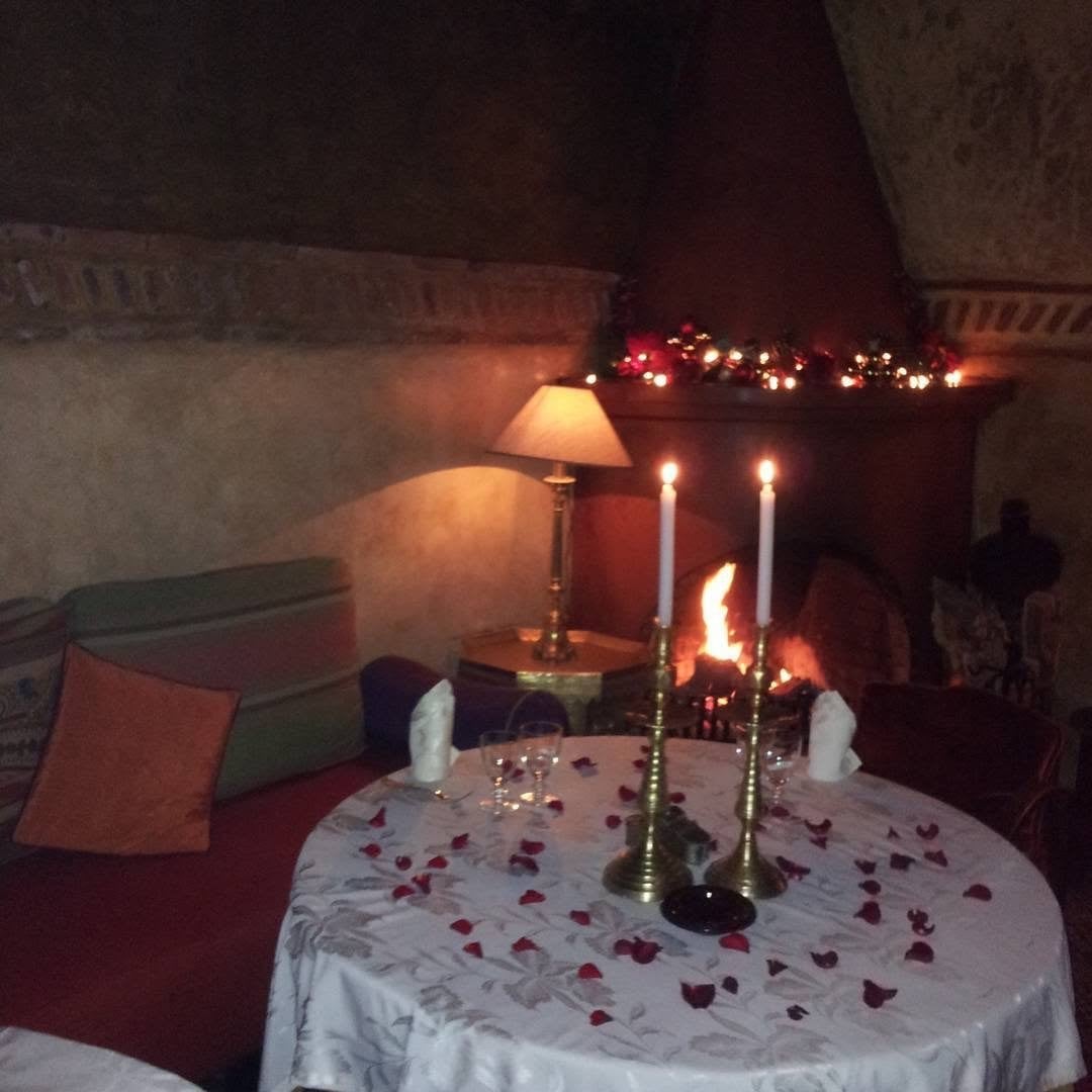 A small salon at Le Tobsil with a lit fireplace, two candles and a table strewn with rose petals