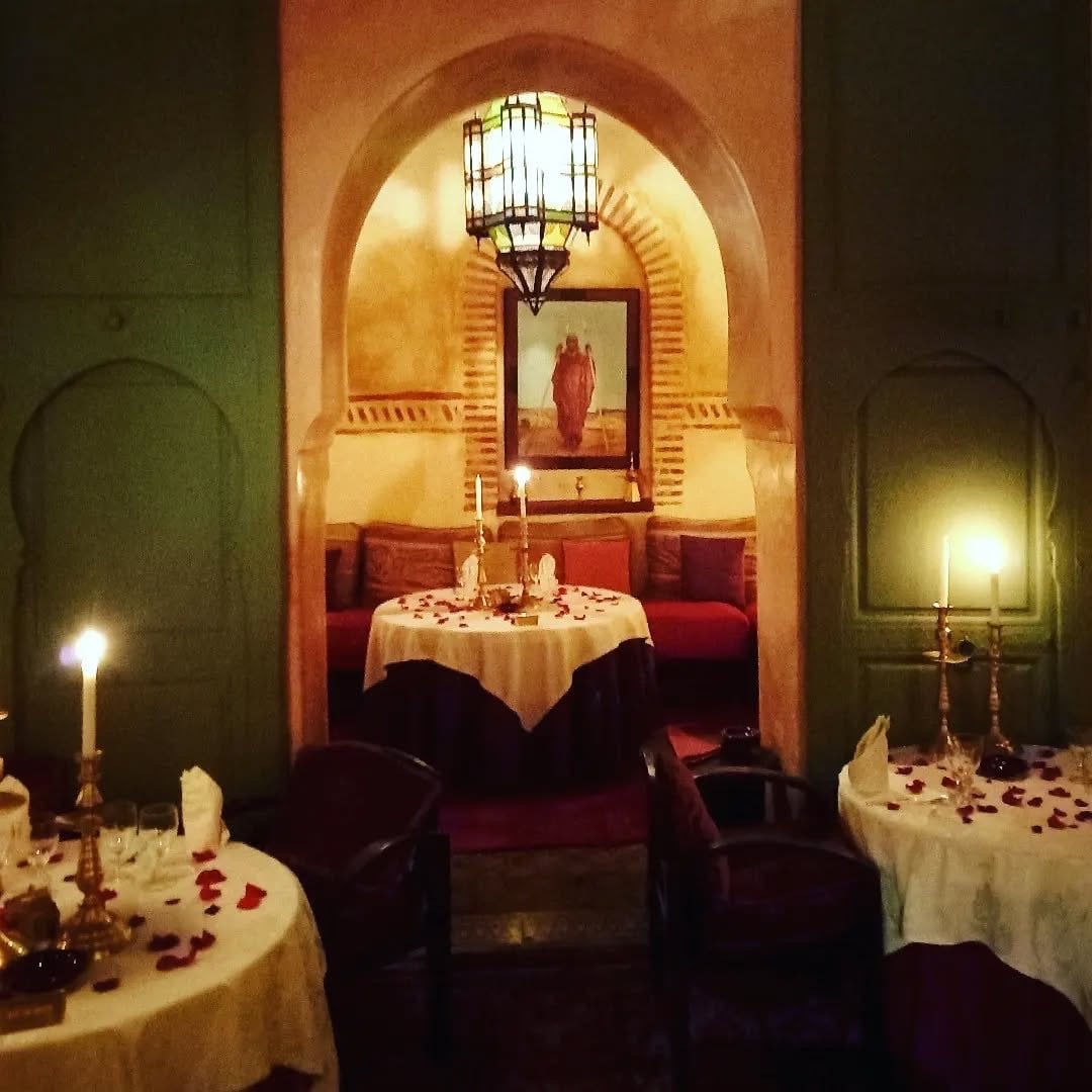A dining room at Le Tobsil under a hanging lantern, a painting in the alcove and candlelit tables around