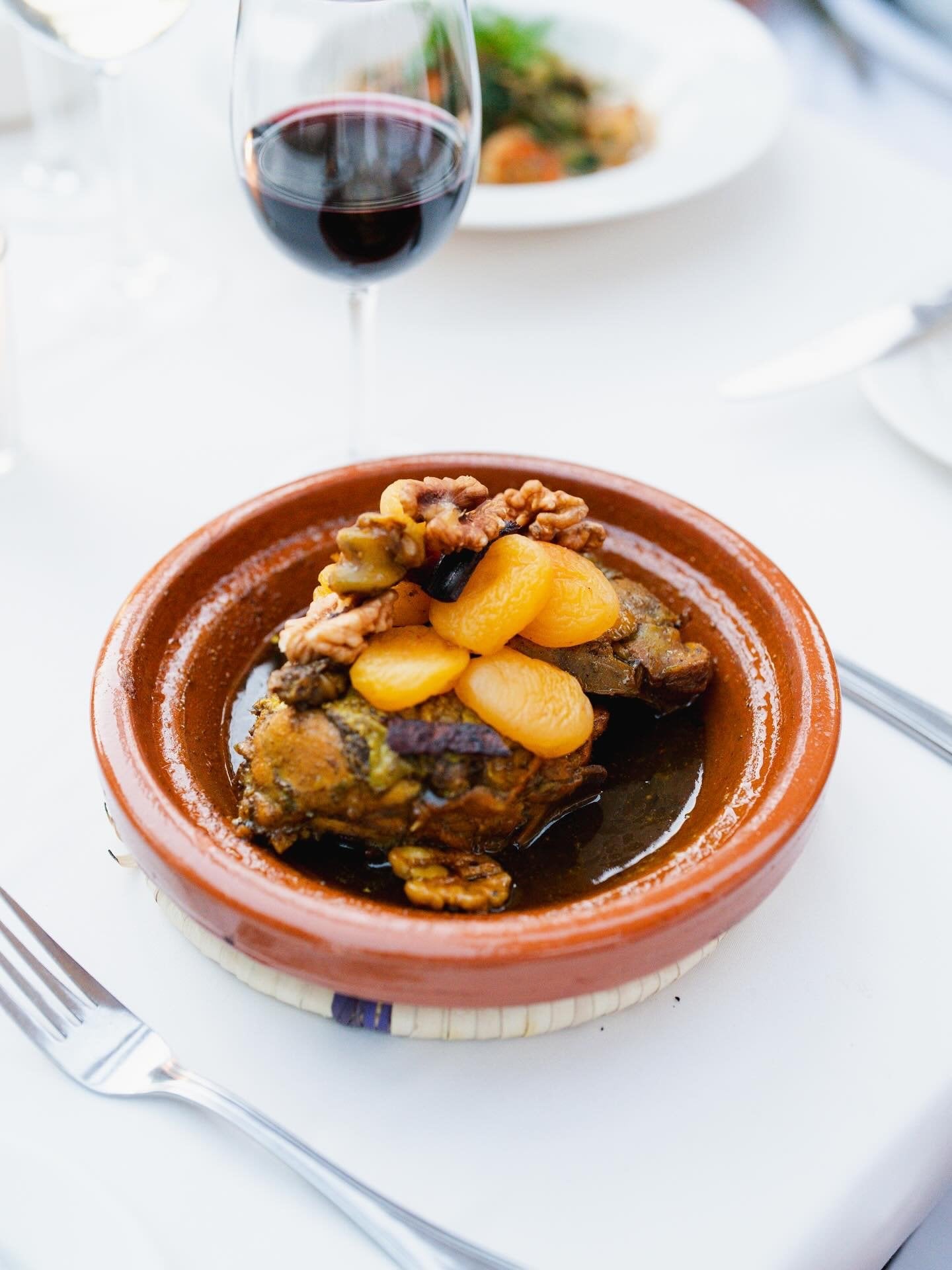 A tagine topped with apricots and walnuts, served with red wine on a white tablecloth at Salammbô